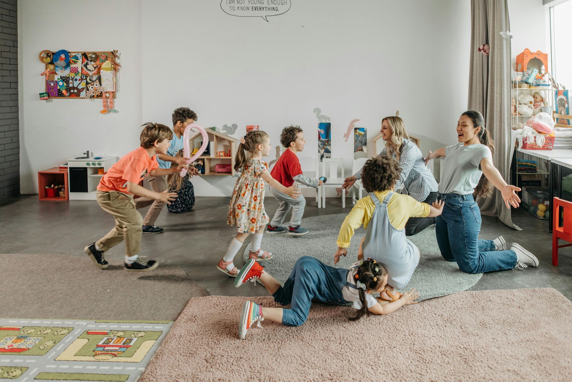 Children playing indoors with a ball in a bright room with rugs and toys.