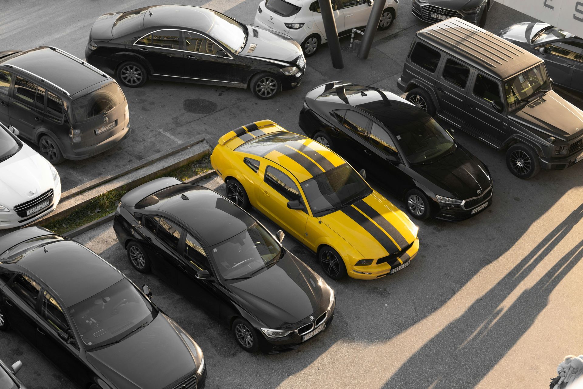 Overhead view of several parked cars, including a yellow sports car, in a lot on a sunny day