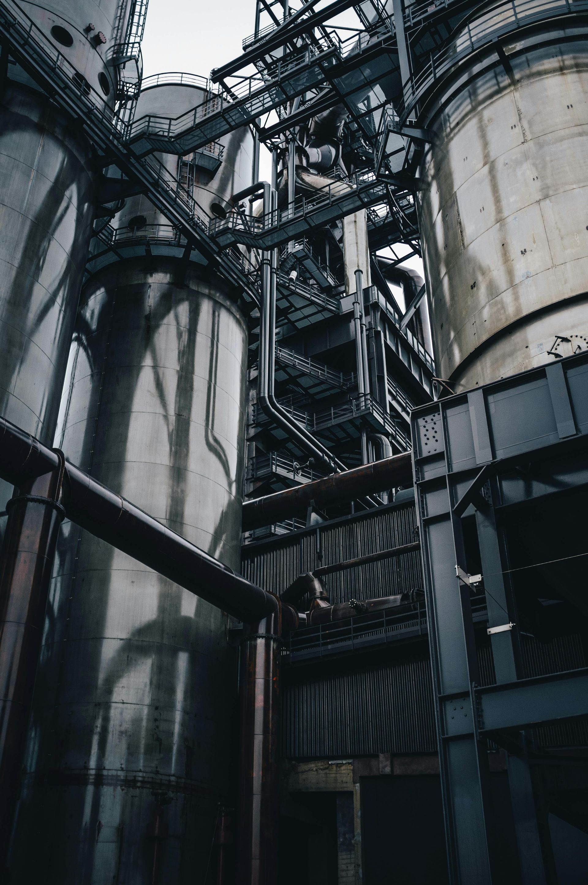 Industrial factory interior with tall metal silos, pipes, and dark steel structures