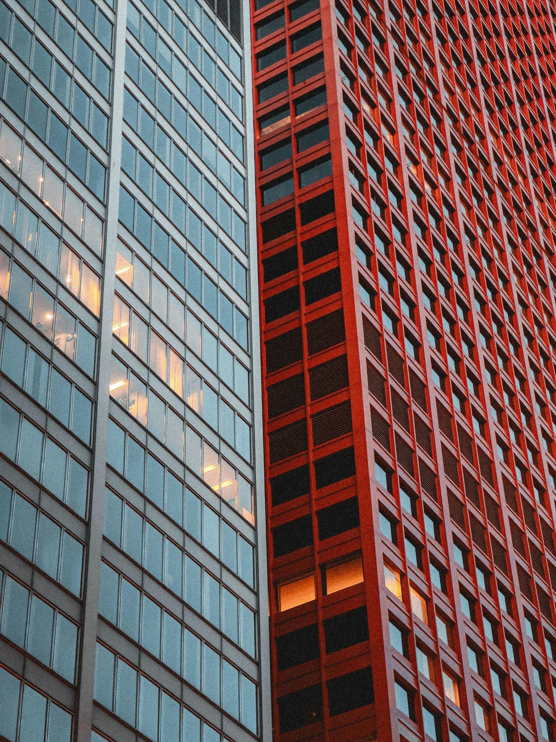 Glass and red high-rise facades at dusk, with lit windows reflecting city light