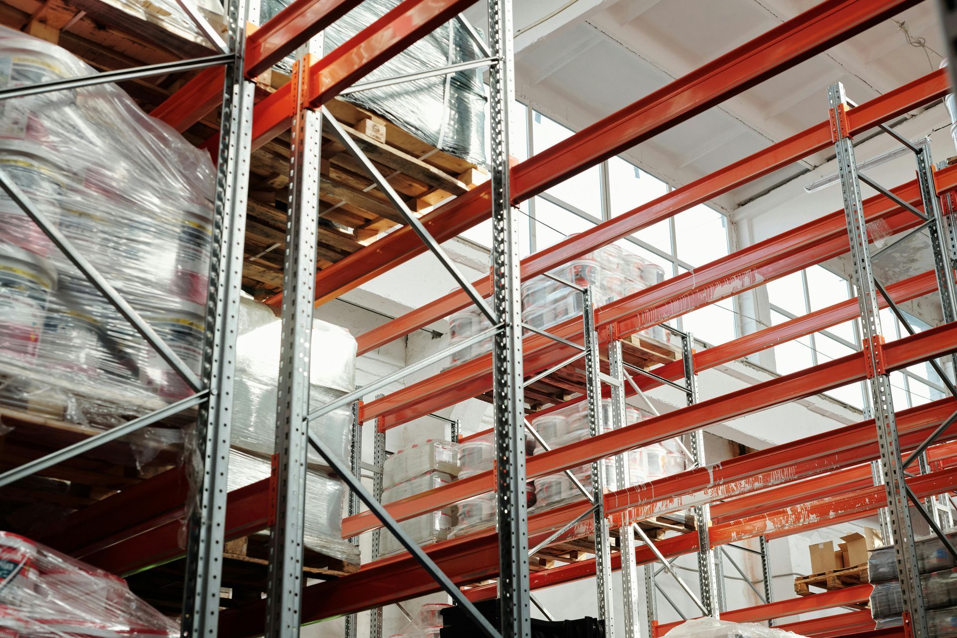 Industrial warehouse shelving with stacked wrapped pallets and red steel racks under bright lights