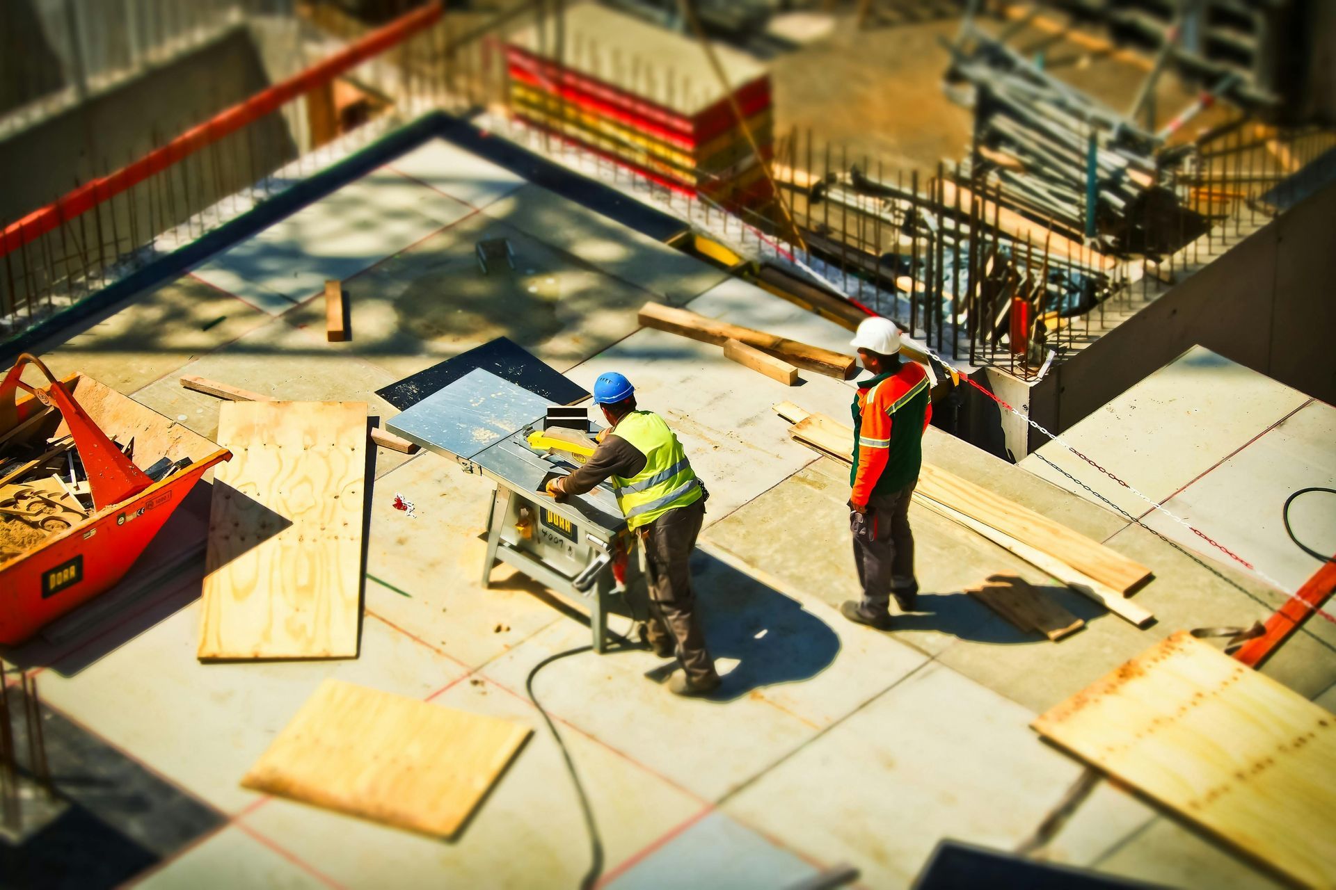 Construction workers measuring plywood on a building site with tools and scaffolding nearby