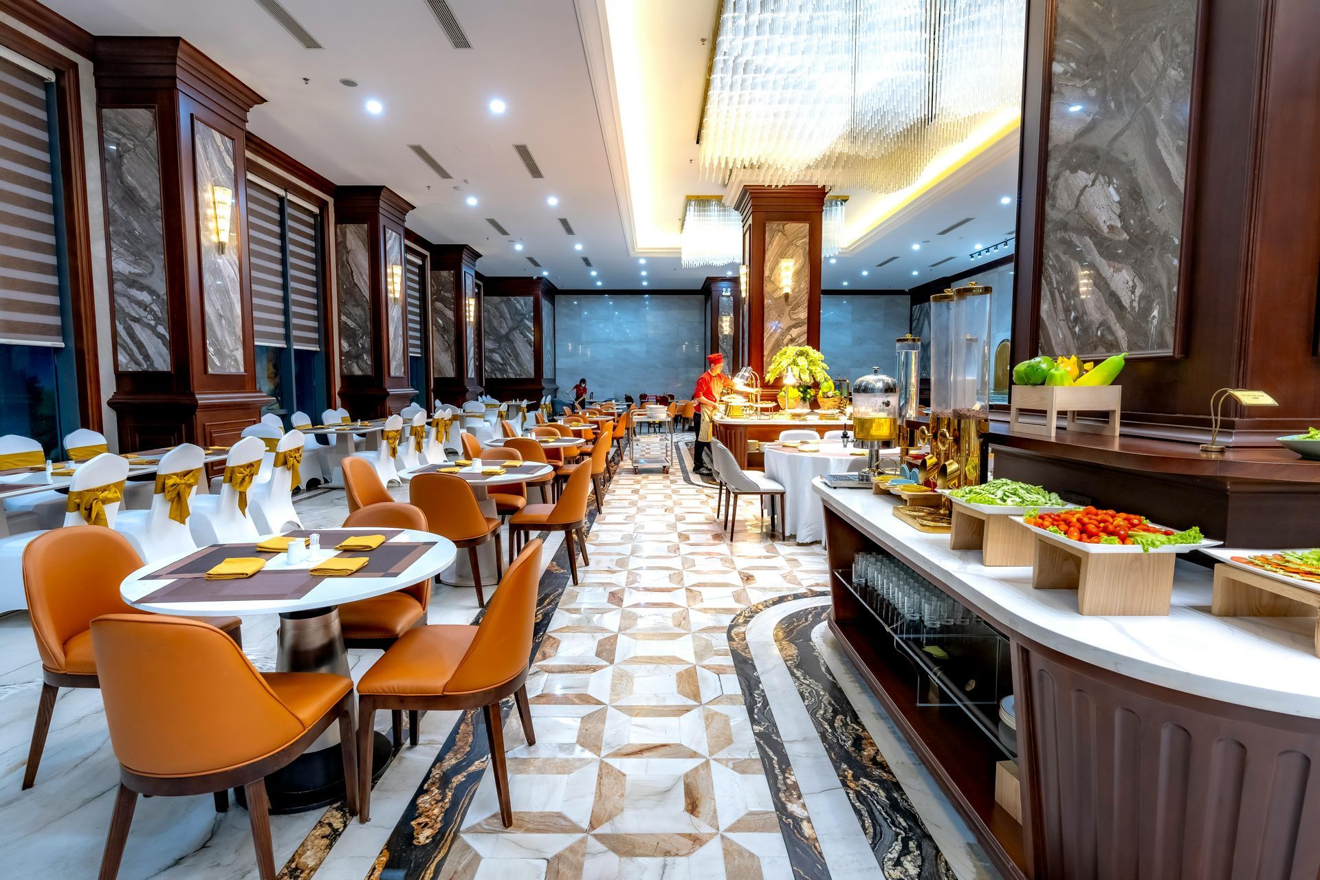 Modern hotel buffet with dining tables, warm lighting, and a long food display counter