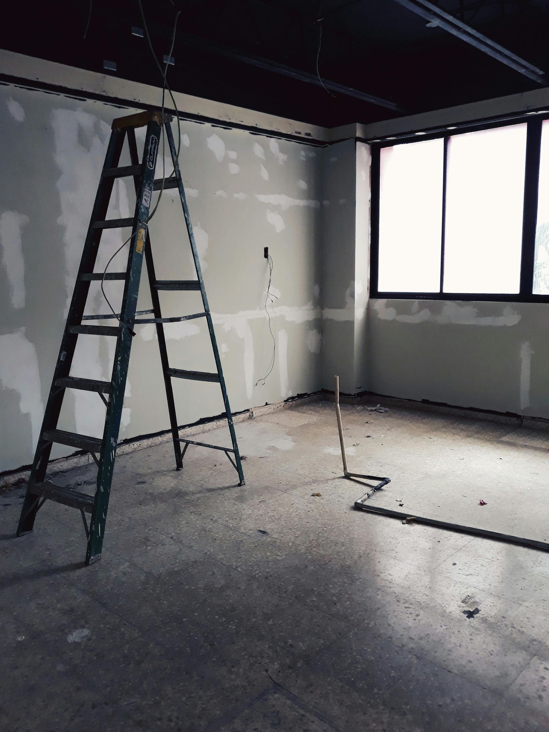 Empty room under renovation with a ladder, unfinished drywall, and a window letting in light