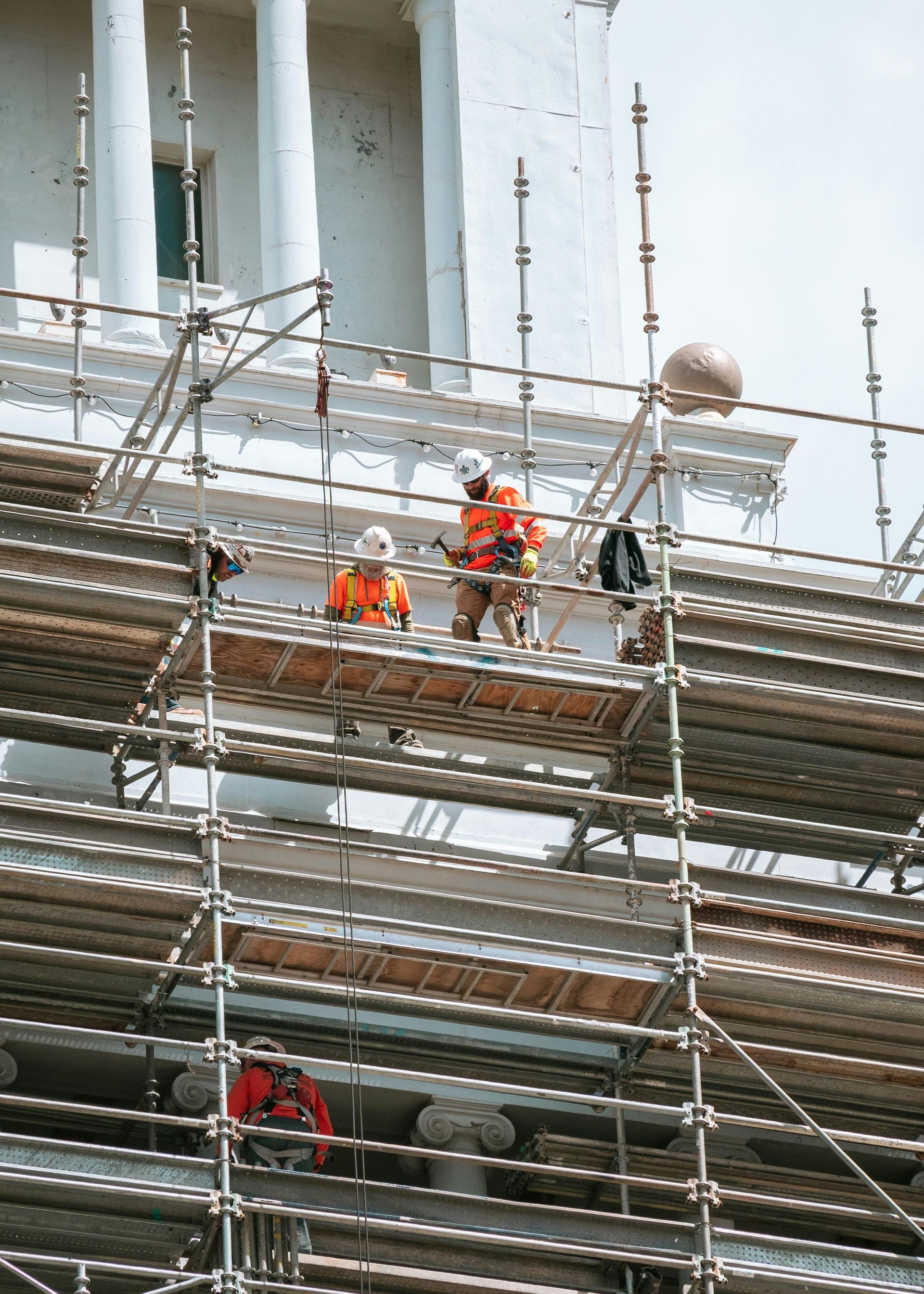 Workers in orange safety gear on scaffolding at a construction site.