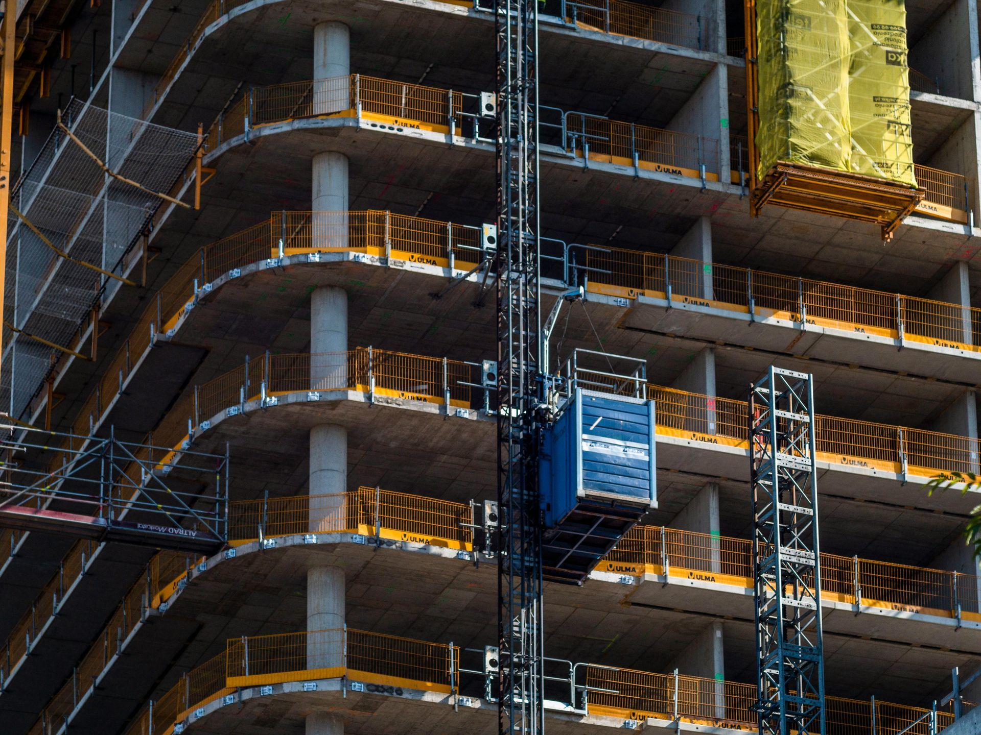 High-rise building under construction with steel scaffolding and a yellow tarp covering part of the facade