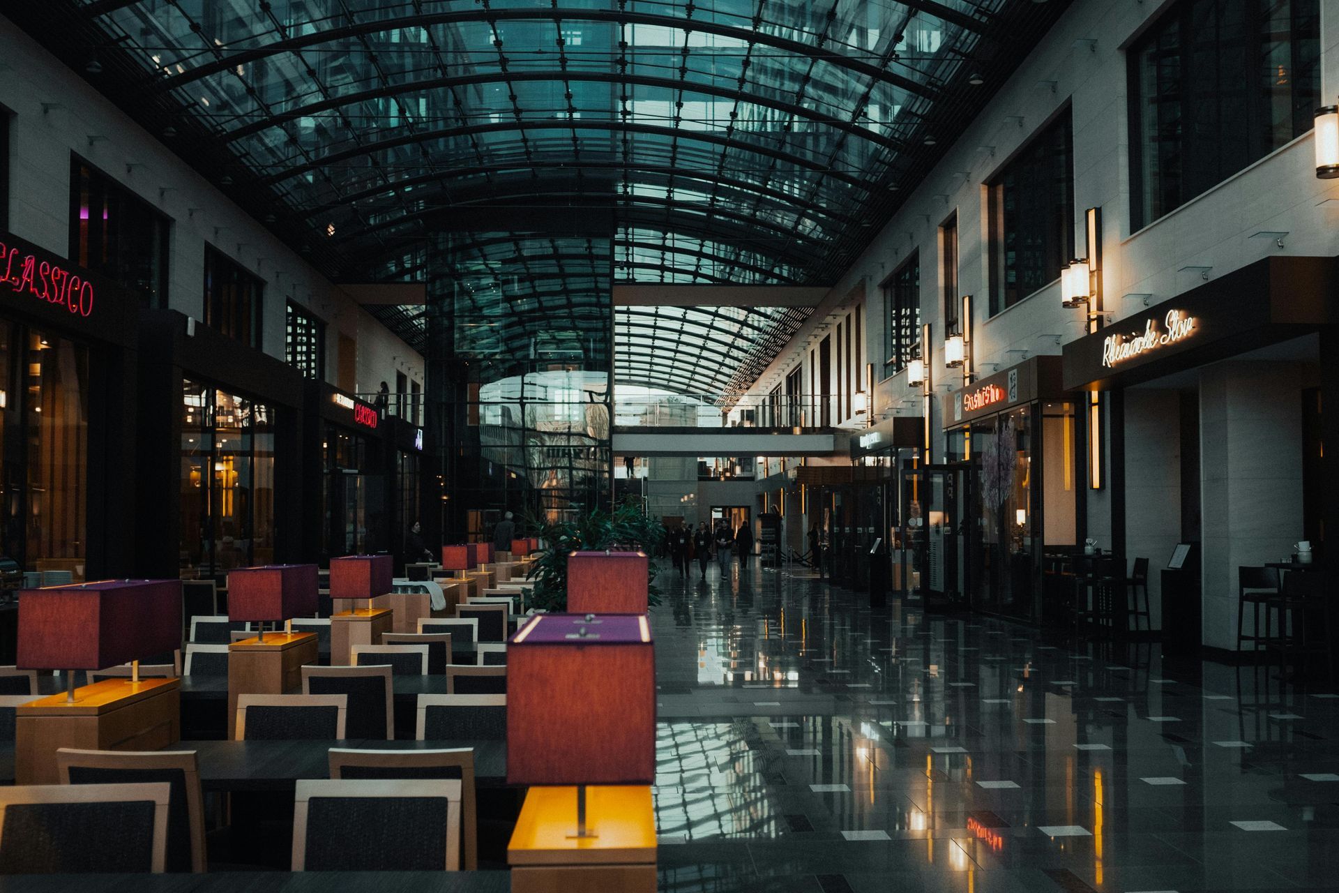 Empty modern atrium with rows of chairs and a glass roof reflecting on polished floors