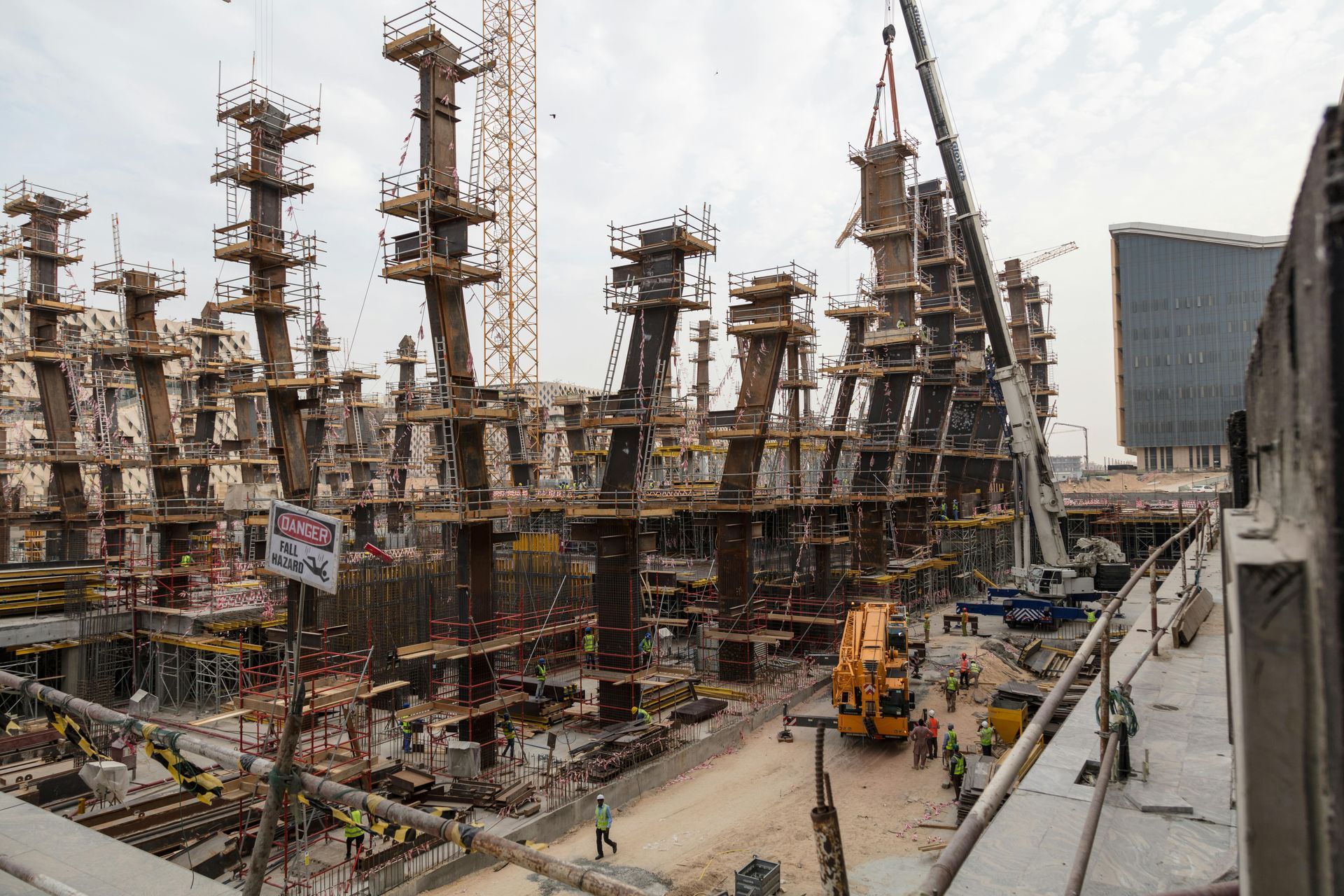 Industrial construction site with steel framework, cranes, and workers in a large urban area