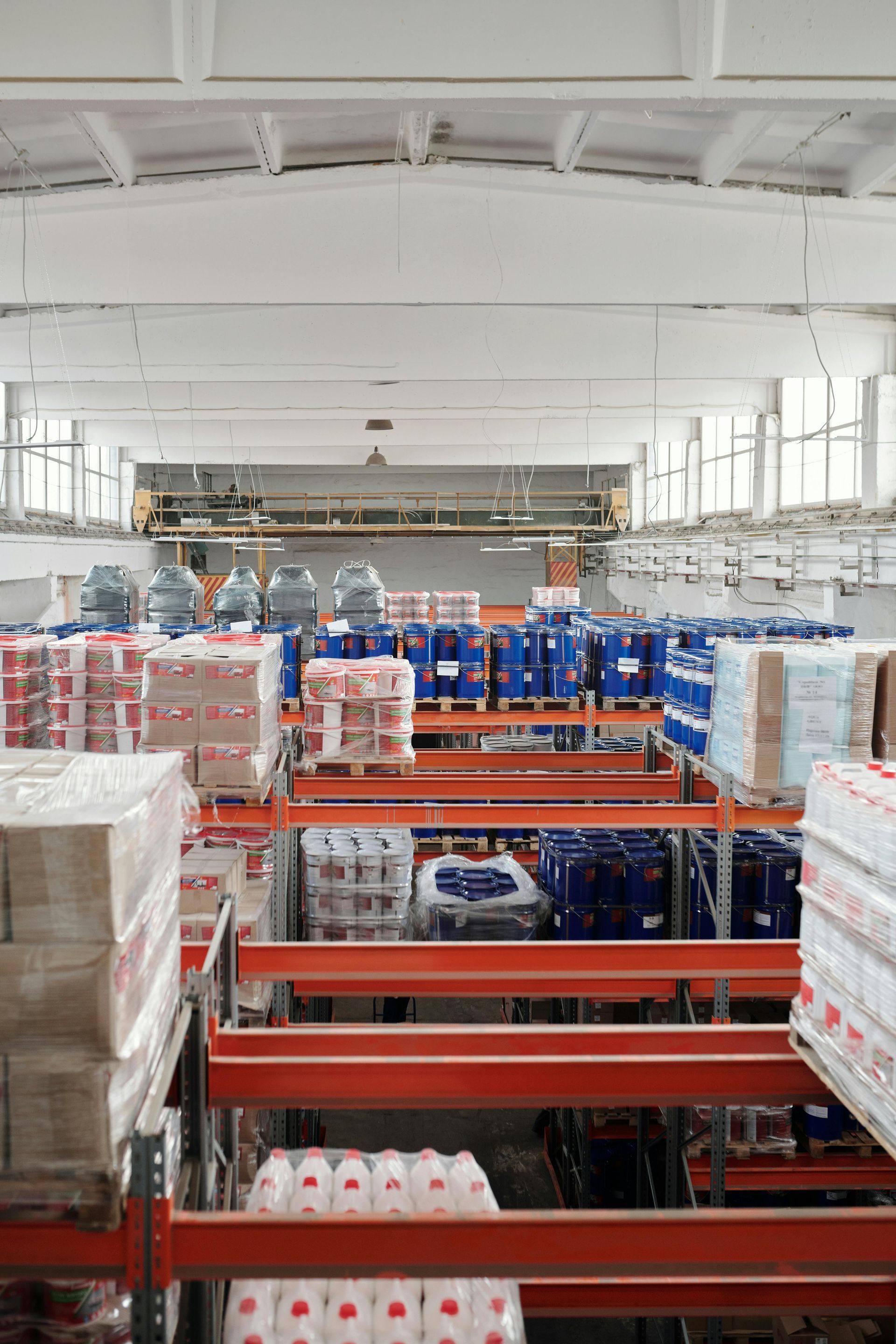 Warehouse aisle with stacked pallets of bottled water and blue-packaged goods on orange racks
