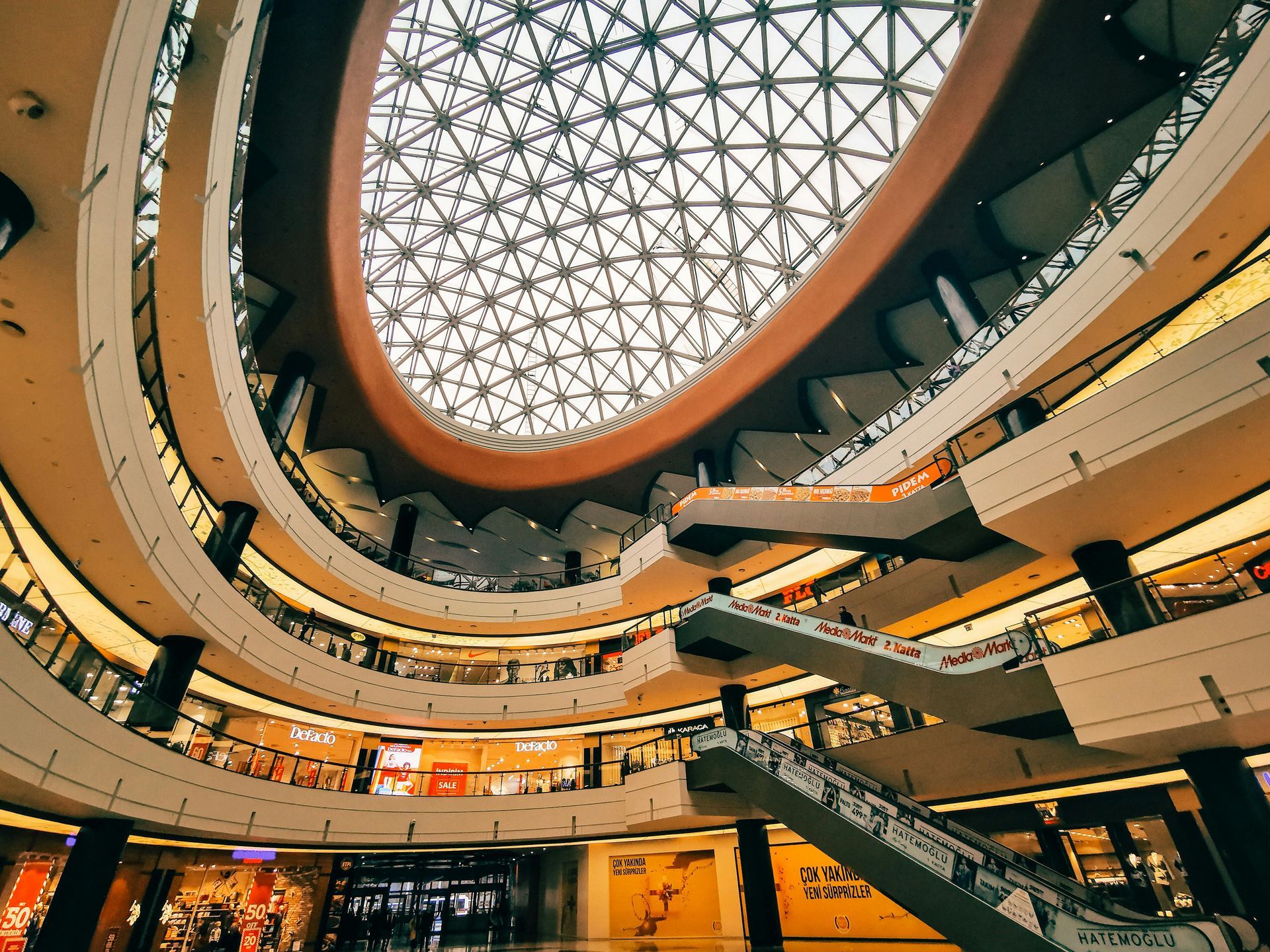 Spacious multi-level mall atrium with a geometric glass dome ceiling and curved balconies