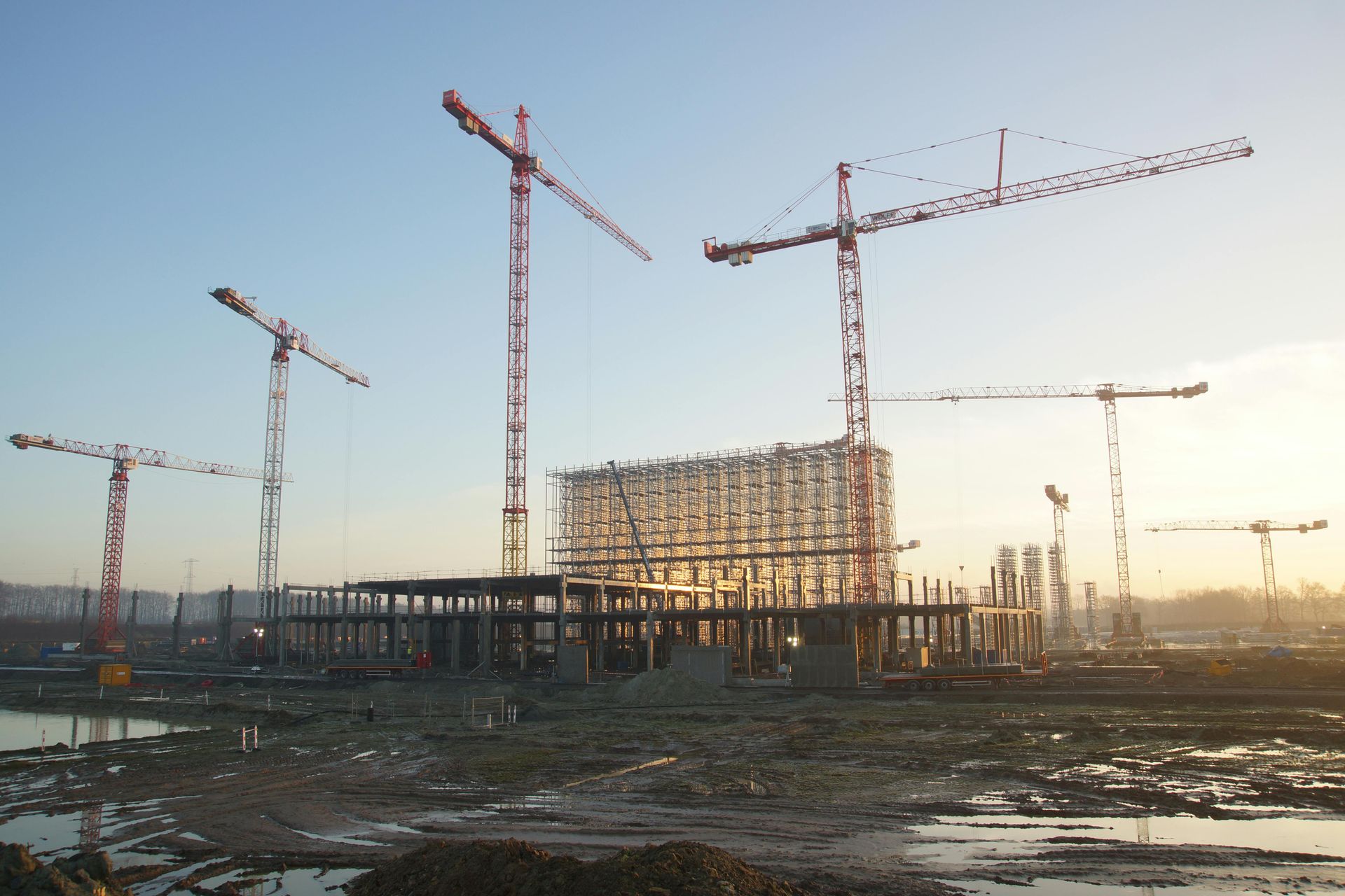 Construction site with multiple cranes and a partially built structure at sunset