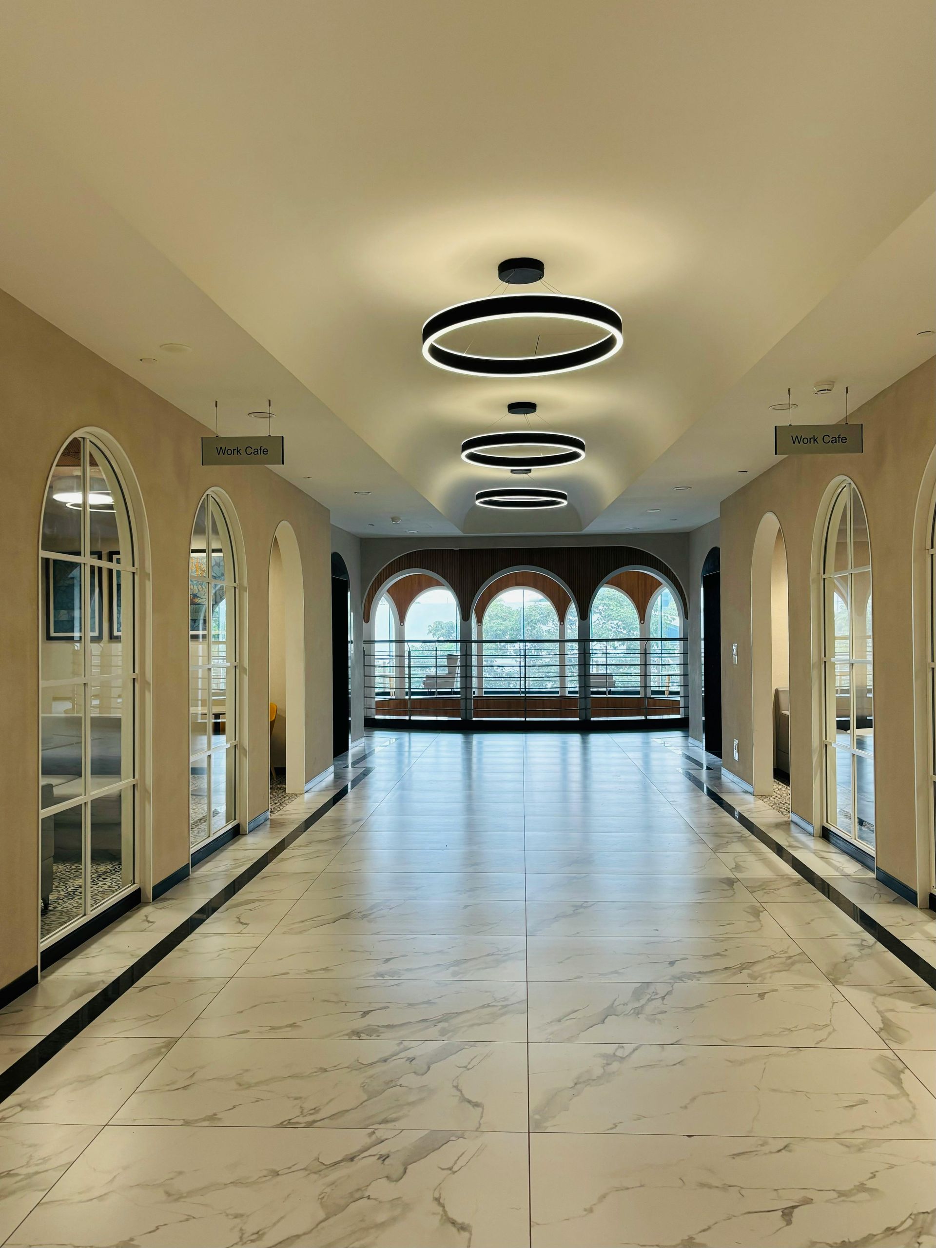 Bright hallway with marble floor, arched mirrors, and ring ceiling lights leading to windows at the far end