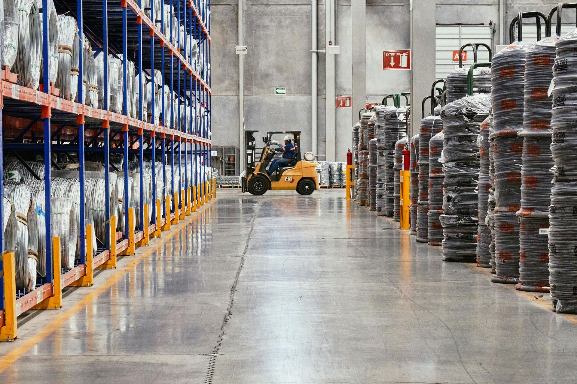 Warehouse aisle with forklift, tall shelving, and stacked pallets under bright lights