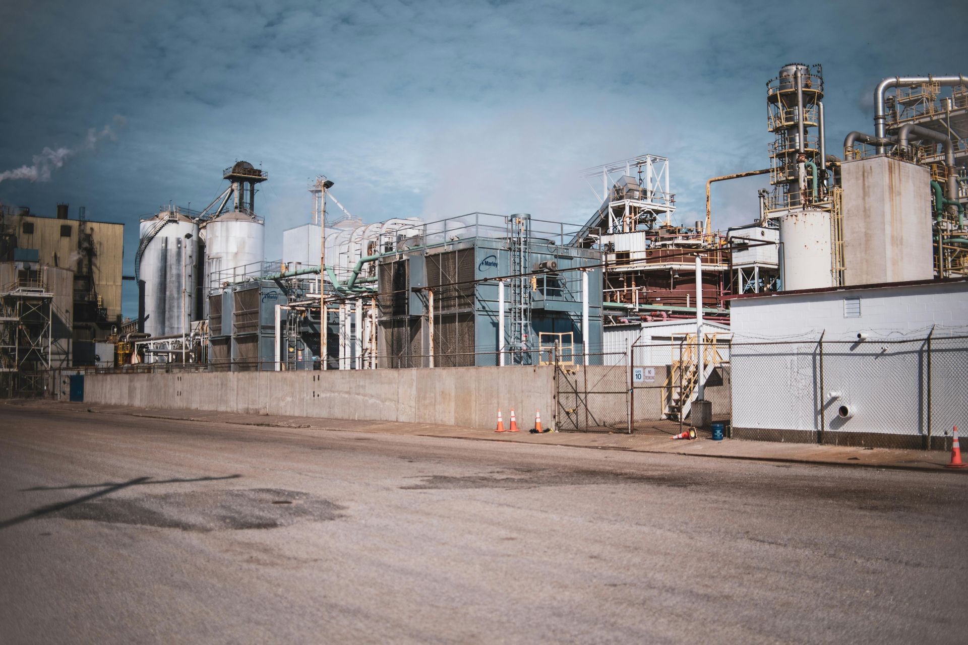 Industrial plant with tanks, pipes, and a fenced yard under a cloudy sky