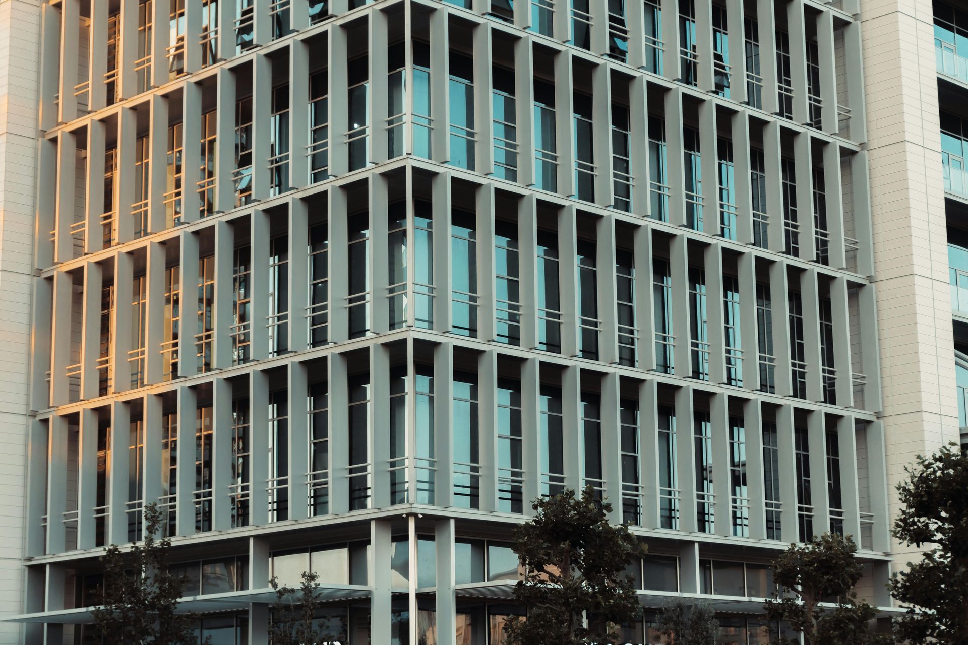 Modern glass office building with white vertical fins and trees in front