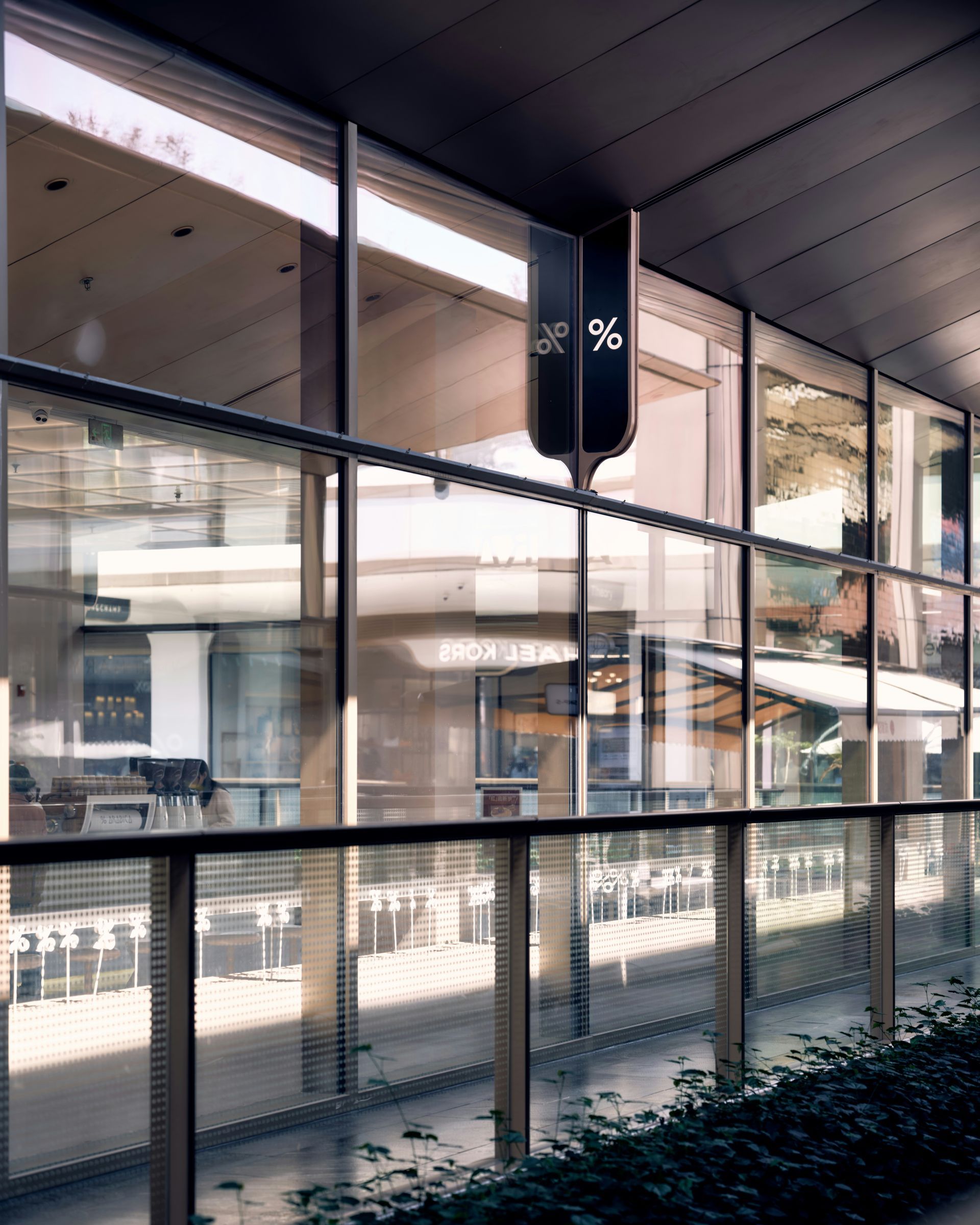 Modern glass-front building with reflections and a covered walkway along the exterior