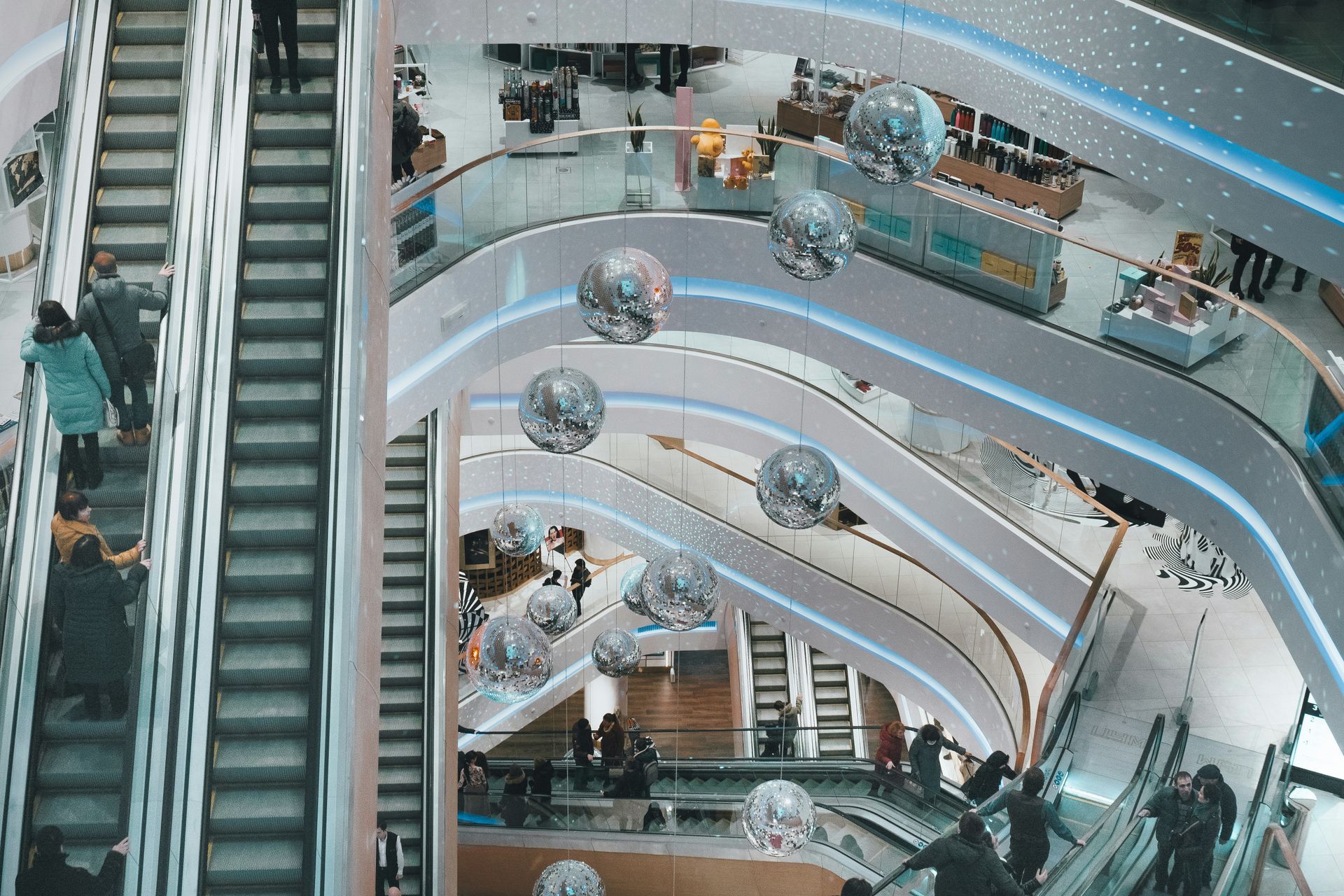 Multi-level shopping mall with escalators, curved balconies, and hanging silver sphere decorations