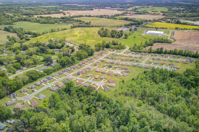 Aerial view of a suburban neighborhood surrounded by fields and trees in a rural setting.
