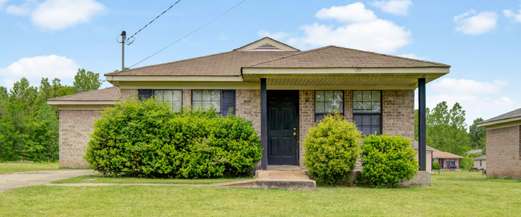 Brick house with green lawn, bushes, and clear sky.