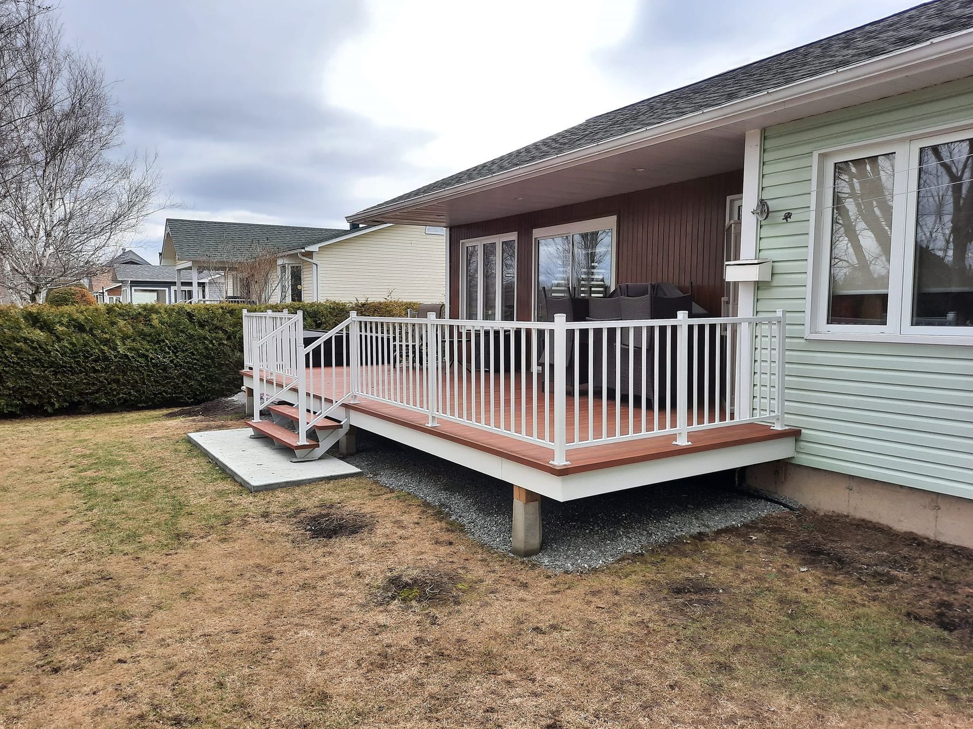 Deck with white railings and brown deck boards, attached to a light green house.