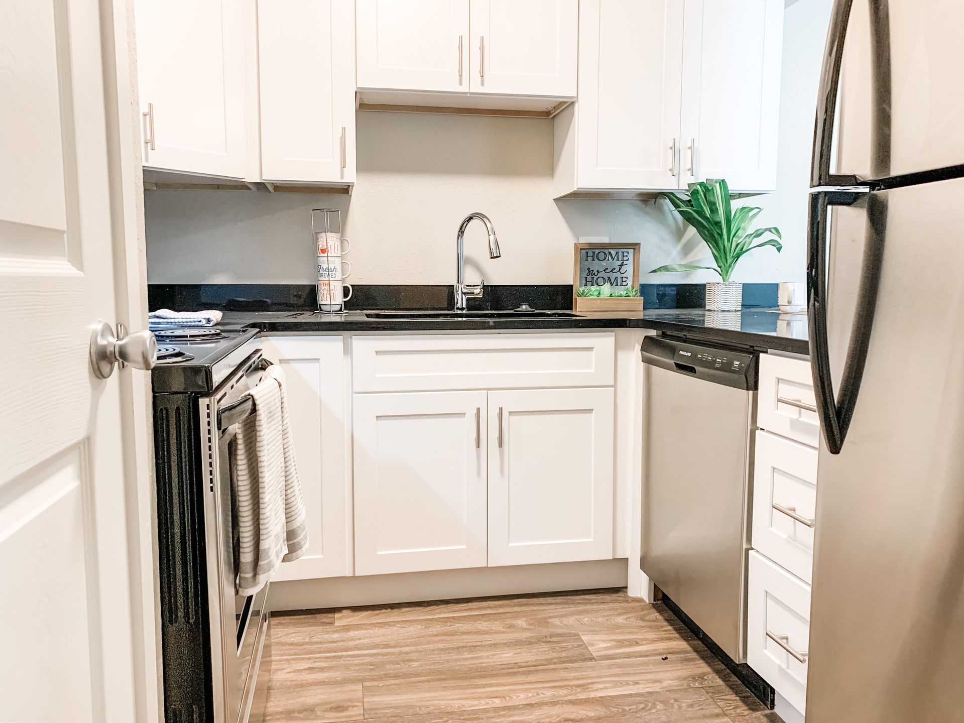 a kitchen with white cabinets , stainless steel appliances , a sink , and a refrigerator .