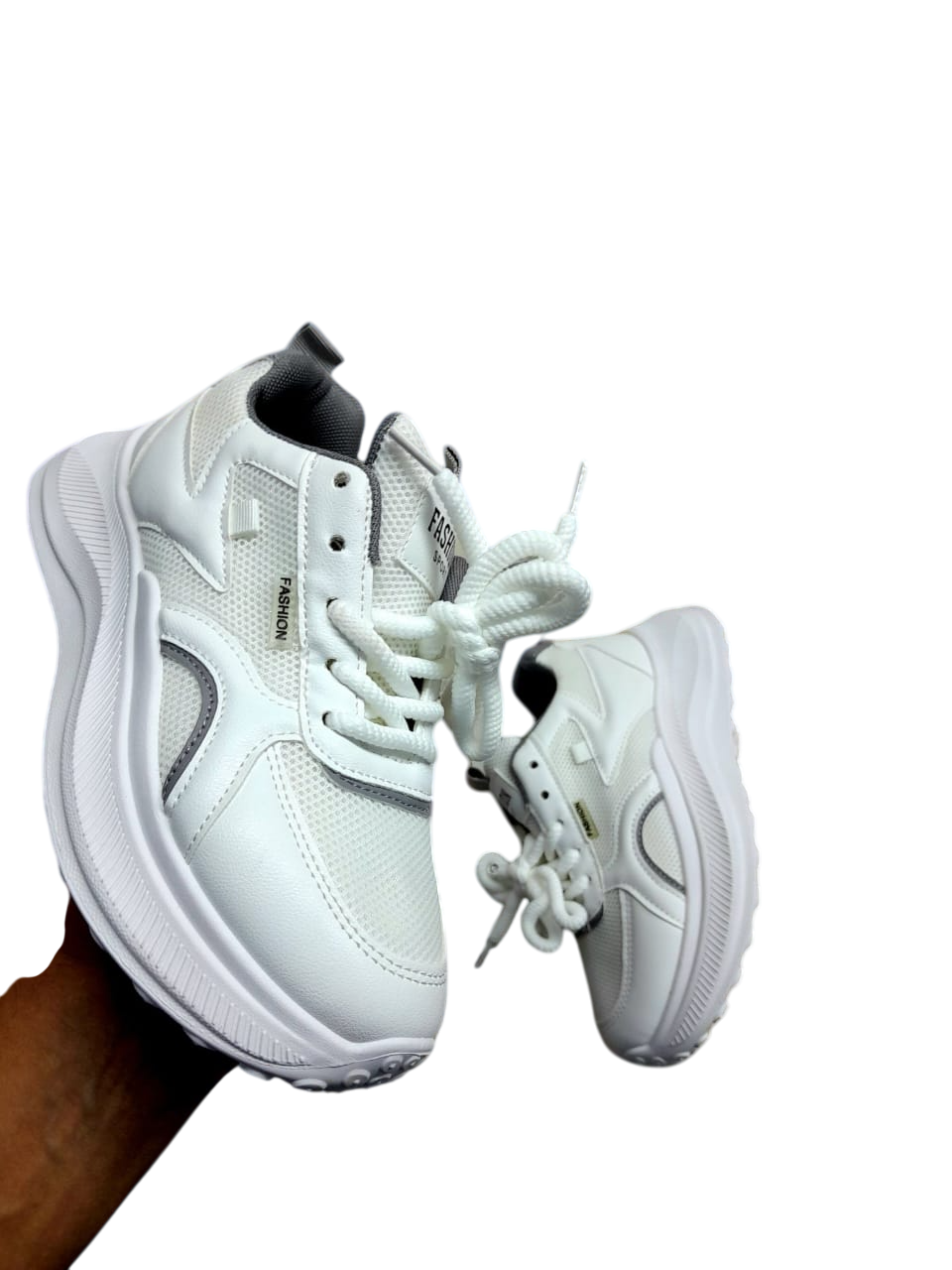 Zapatillas de plataforma blancas con detalles en negro sostenidas por una mano sobre un fondo blanco.