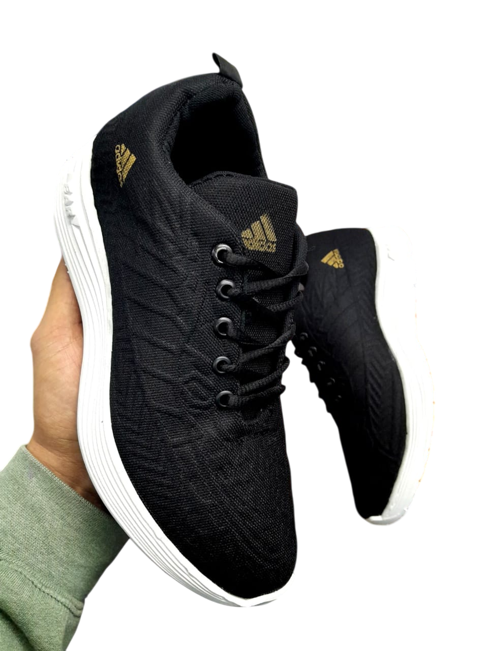 Una persona sostiene unas zapatillas Adidas negras con suelas blancas sobre un fondo blanco.