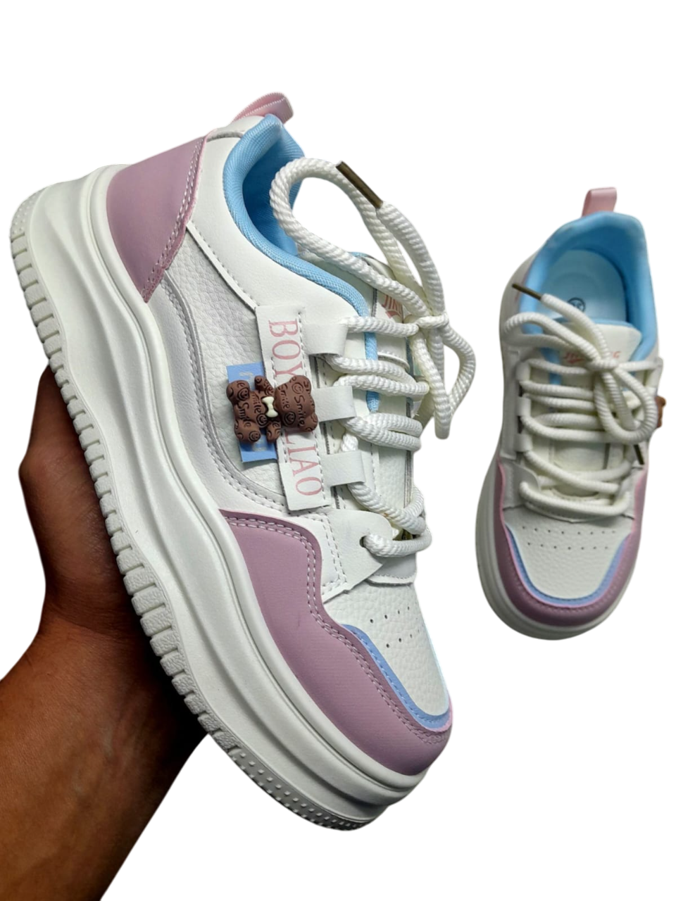 Zapatillas blancas y azul marino con suela gruesa blanca, sujetas con una mano. Texto