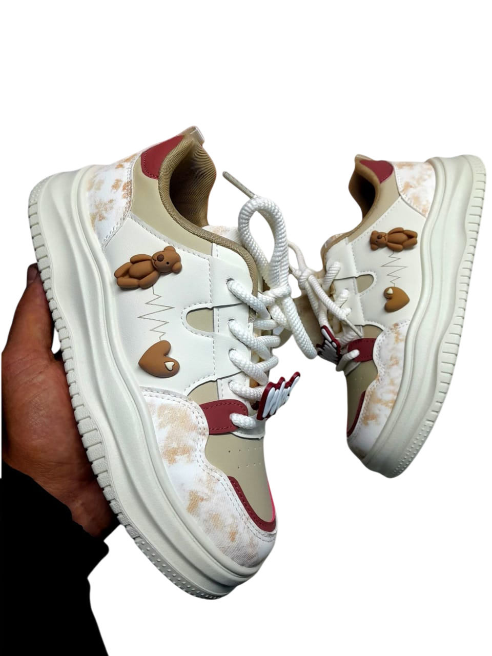 Zapatillas color crema y rojo con adornos de osito y corazón. Sostenidas por una persona.