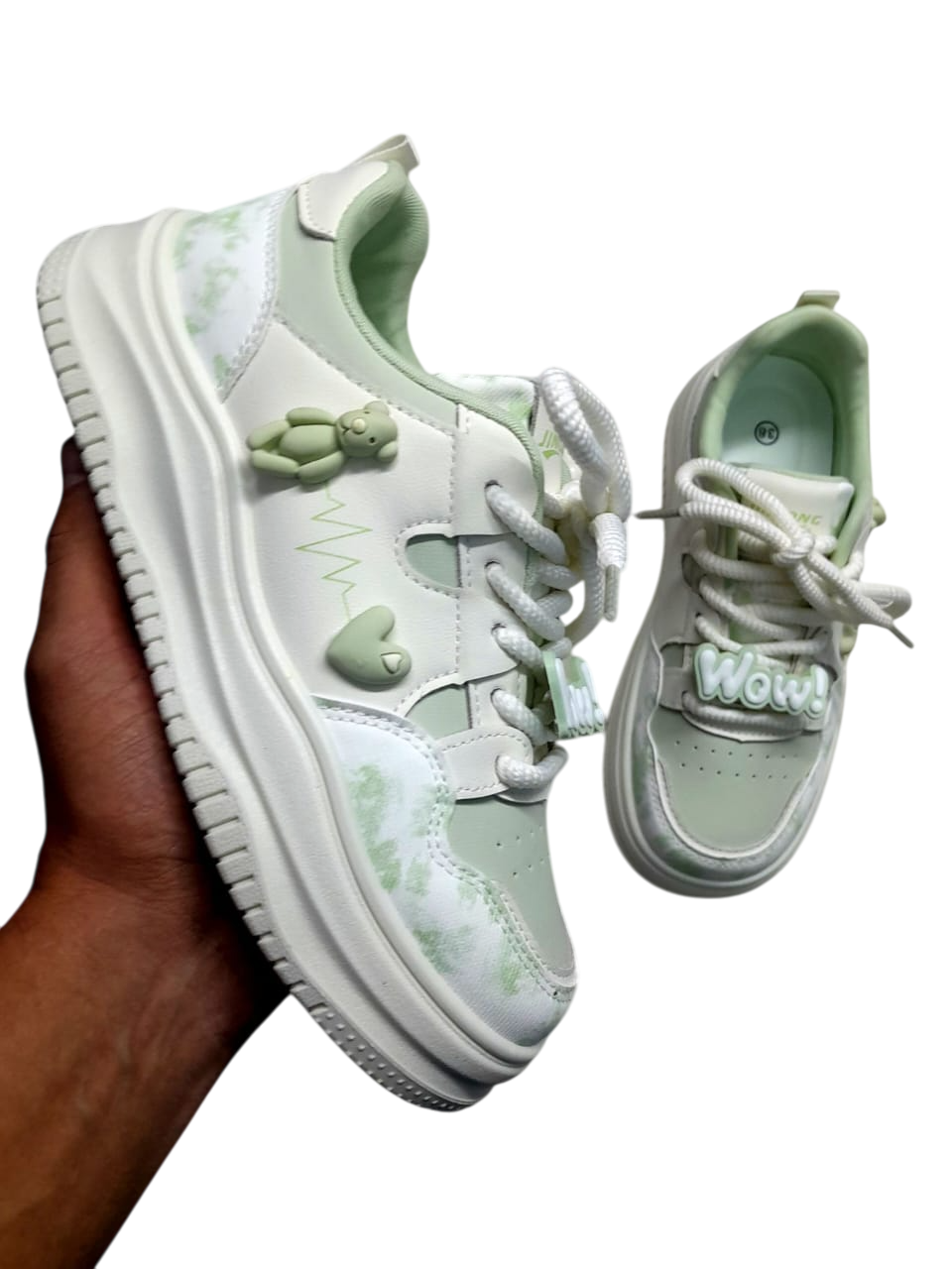 Zapatillas color crema y rojo con adornos de osito y corazón. Sostenidas por una persona.