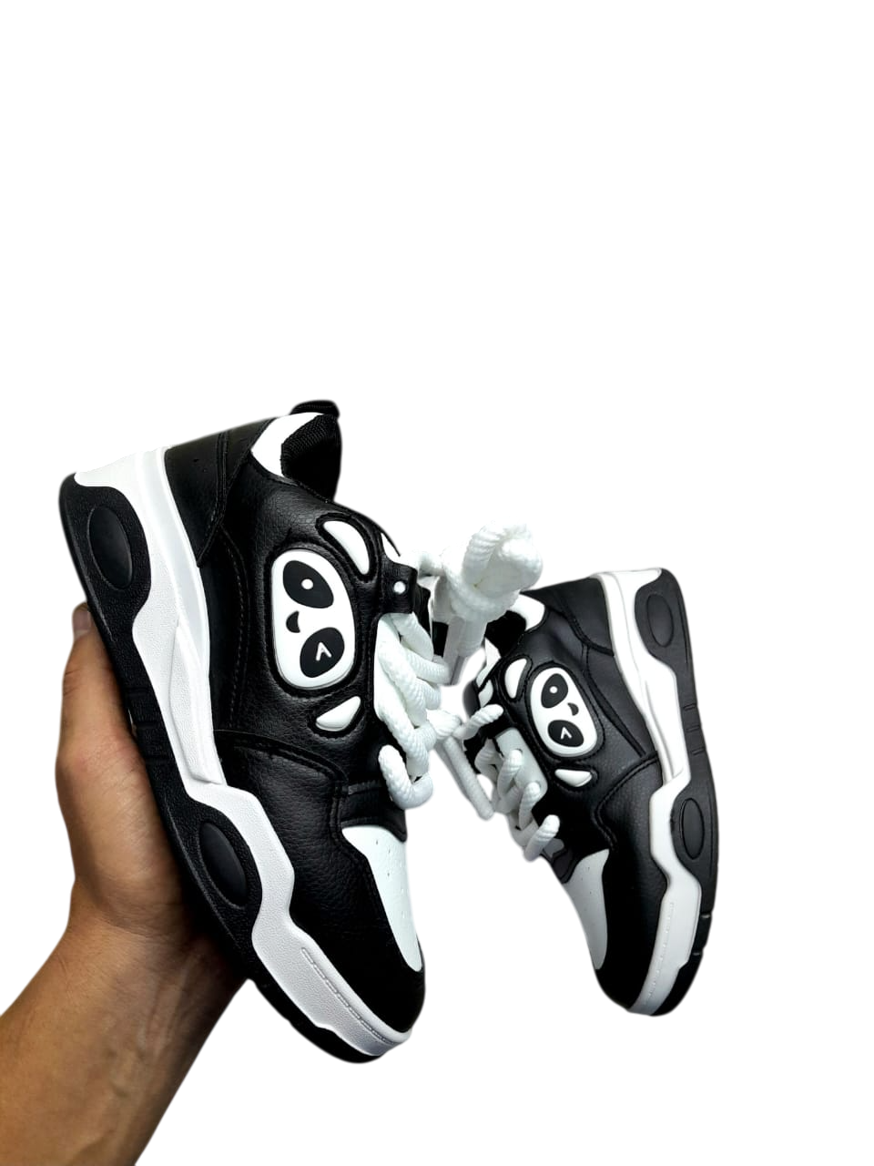 Zapatillas de panda en blanco y negro con detalles rosas, sostenidas en una mano.