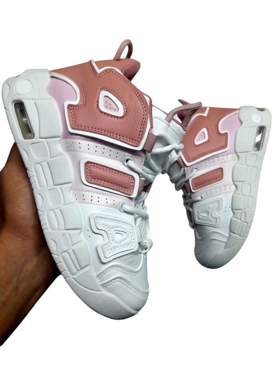 Zapatillas deportivas blancas sostenidas por una mano; ambas zapatillas son blancas y tienen un diseño muy recargado.
