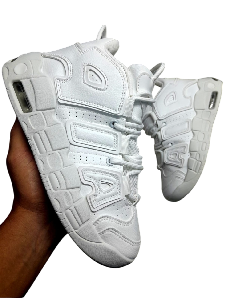 Zapatillas deportivas blancas sostenidas por una mano; ambas zapatillas son blancas y tienen un diseño muy recargado.