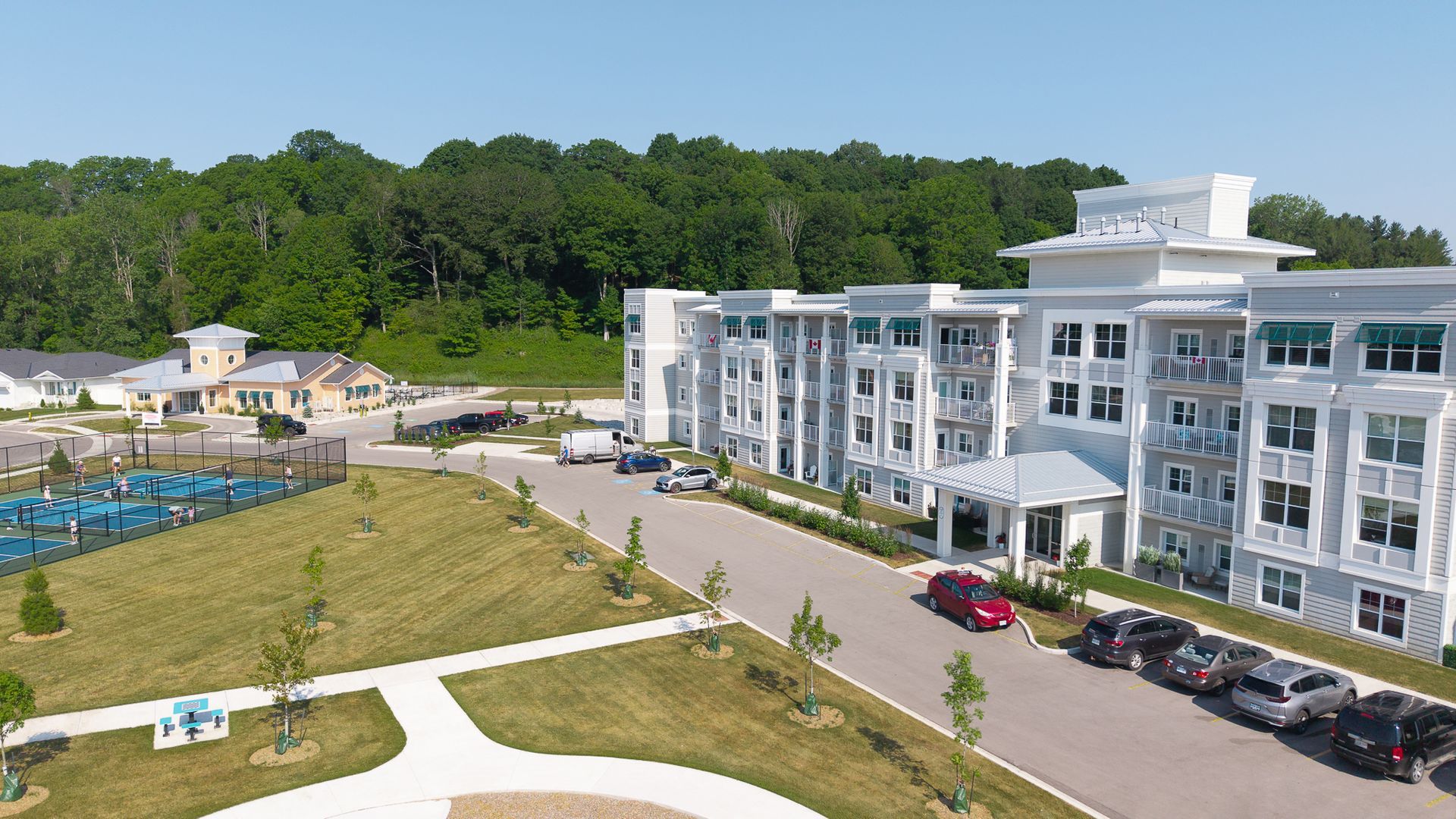 Large modern apartment building, gray and white with balconies, set in a park-like setting with trees.