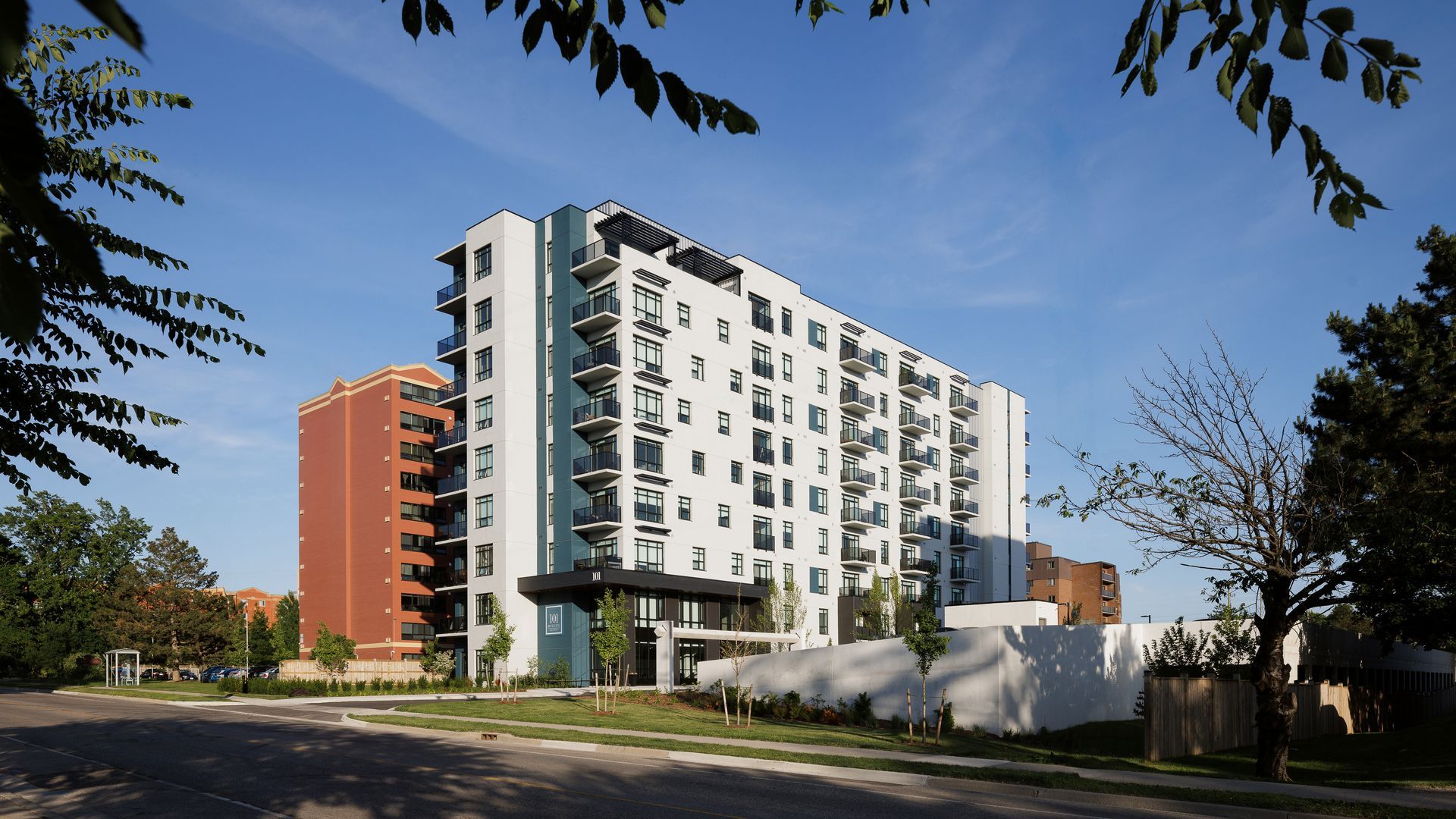 Modern, multi-story apartment building with white and gray facade under a blue sky.