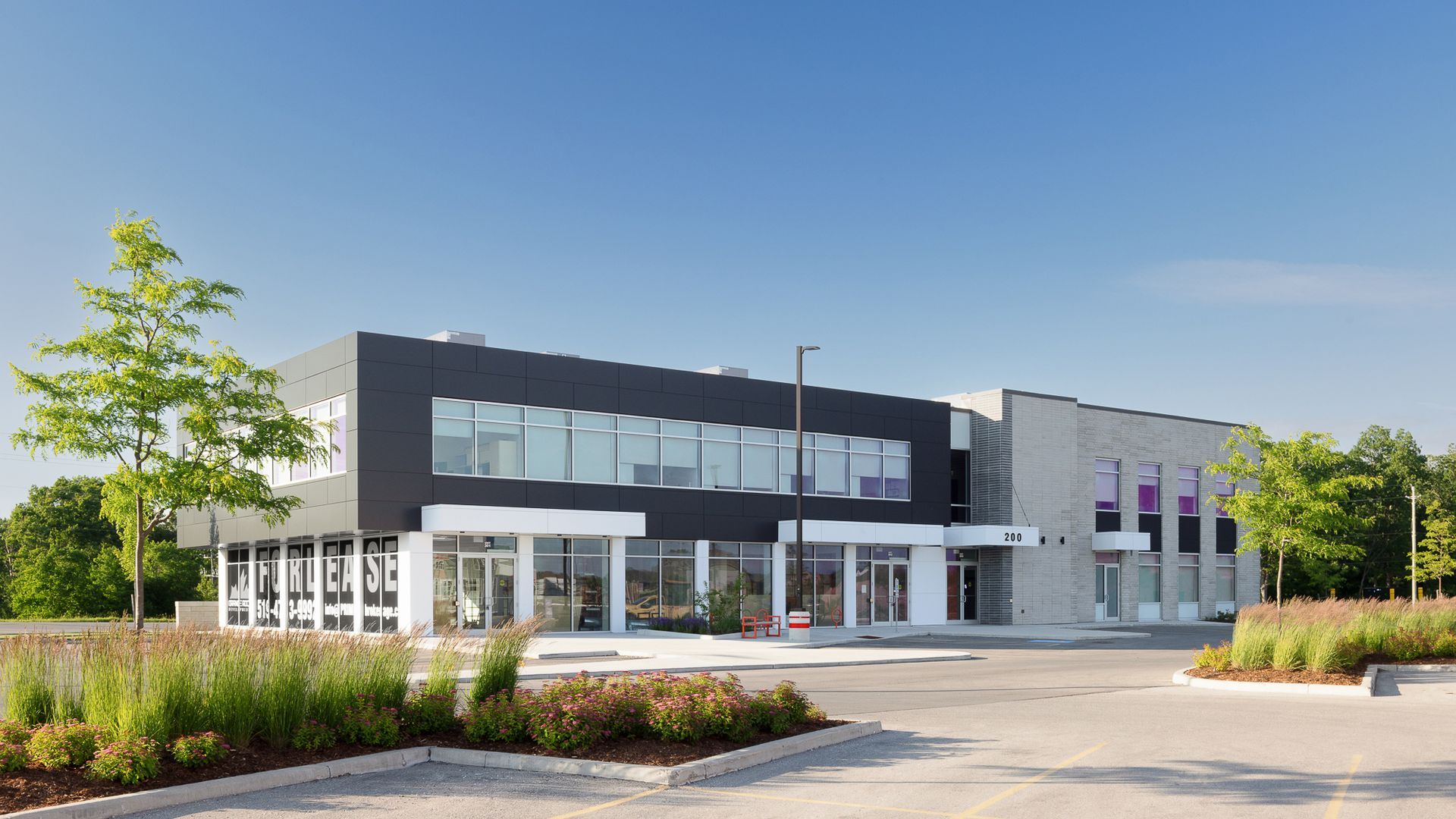 White modern office building with landscaping and cars on a nearby road under a blue sky.