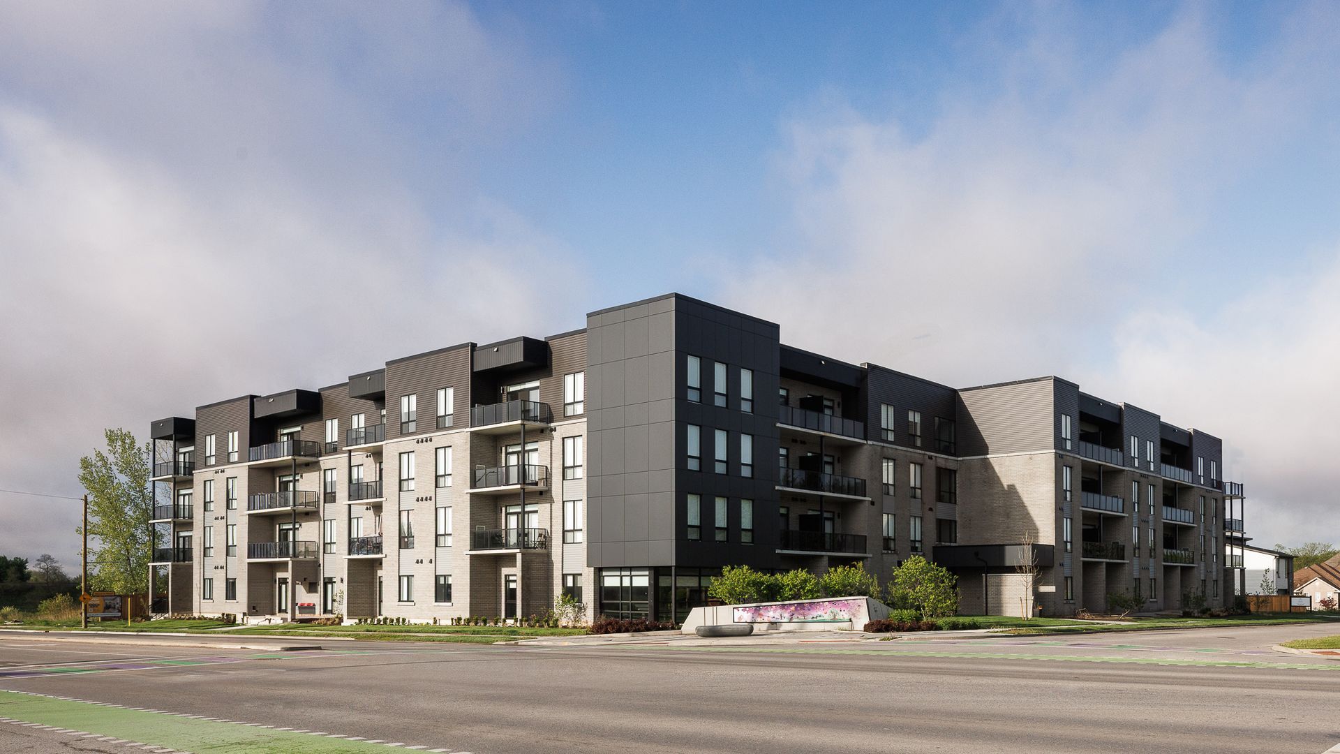Modern multi-story apartment building with dark gray and light gray exterior under a cloudy sky.