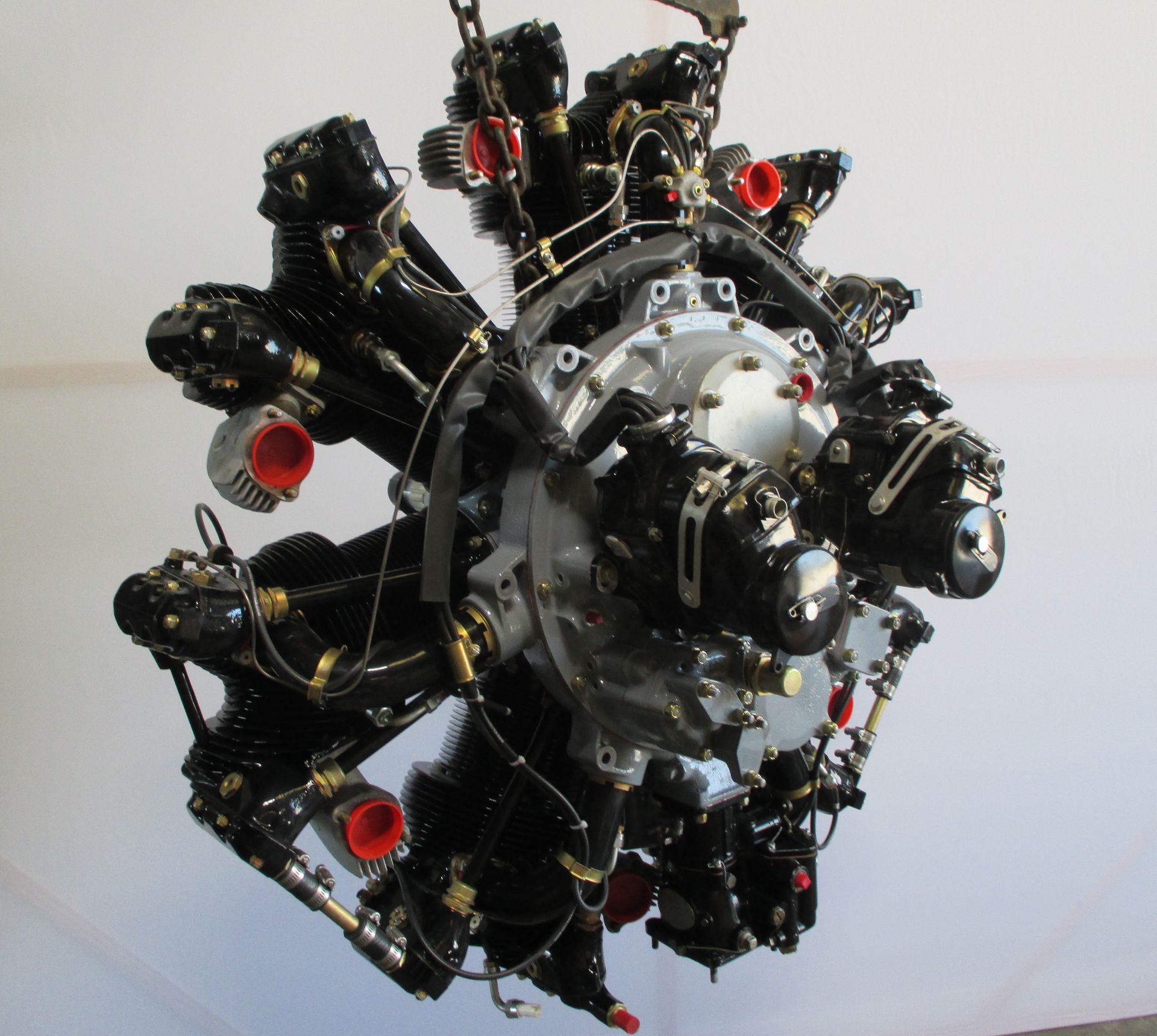 A large engine is hanging from a chain on a white wall