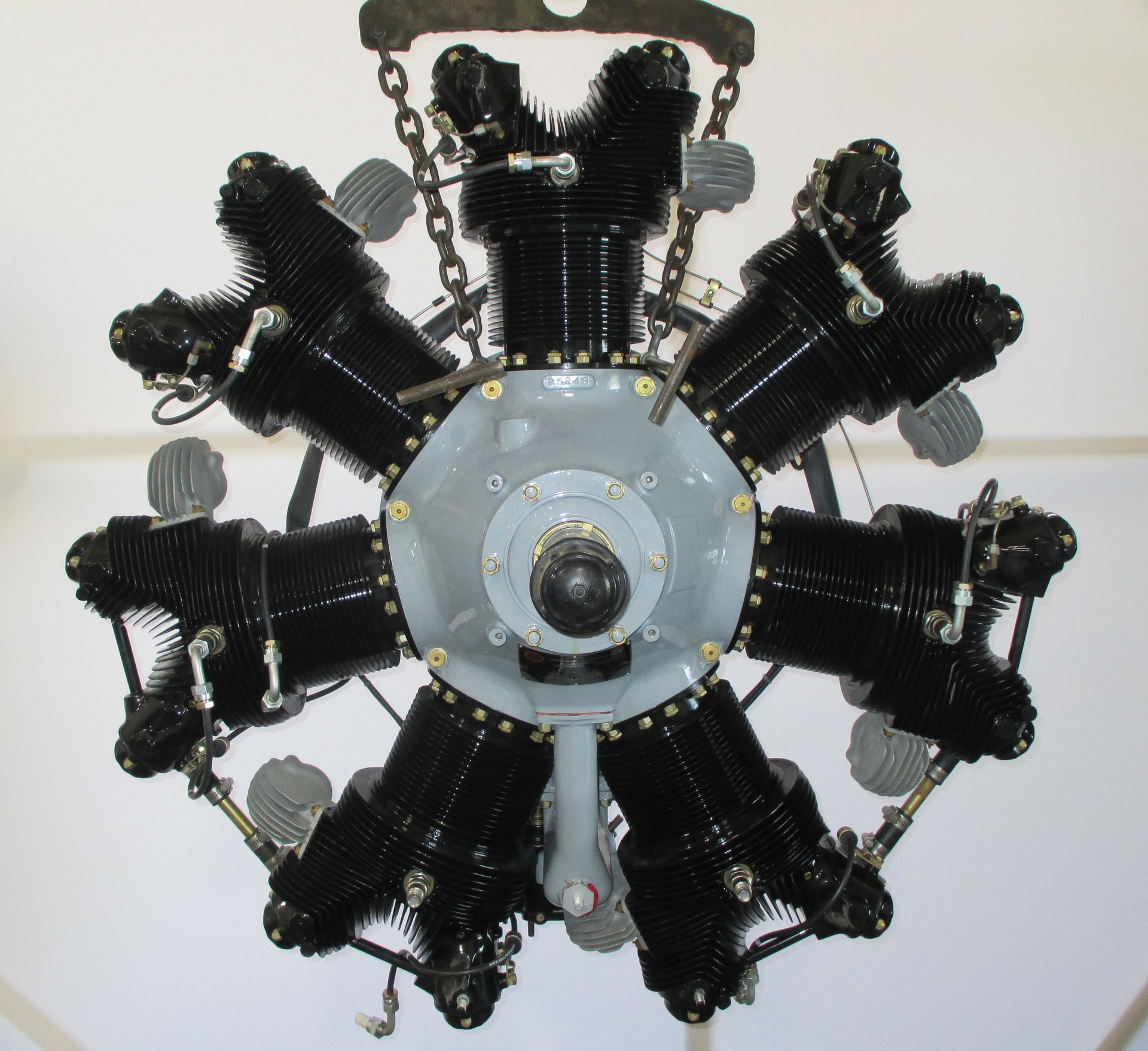 A large black engine is hanging from chains on a white wall