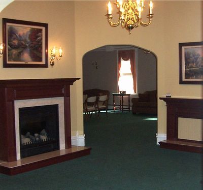 A room with dark wood fireplaces, arched doorway, and chandelier; green carpet, cream walls.