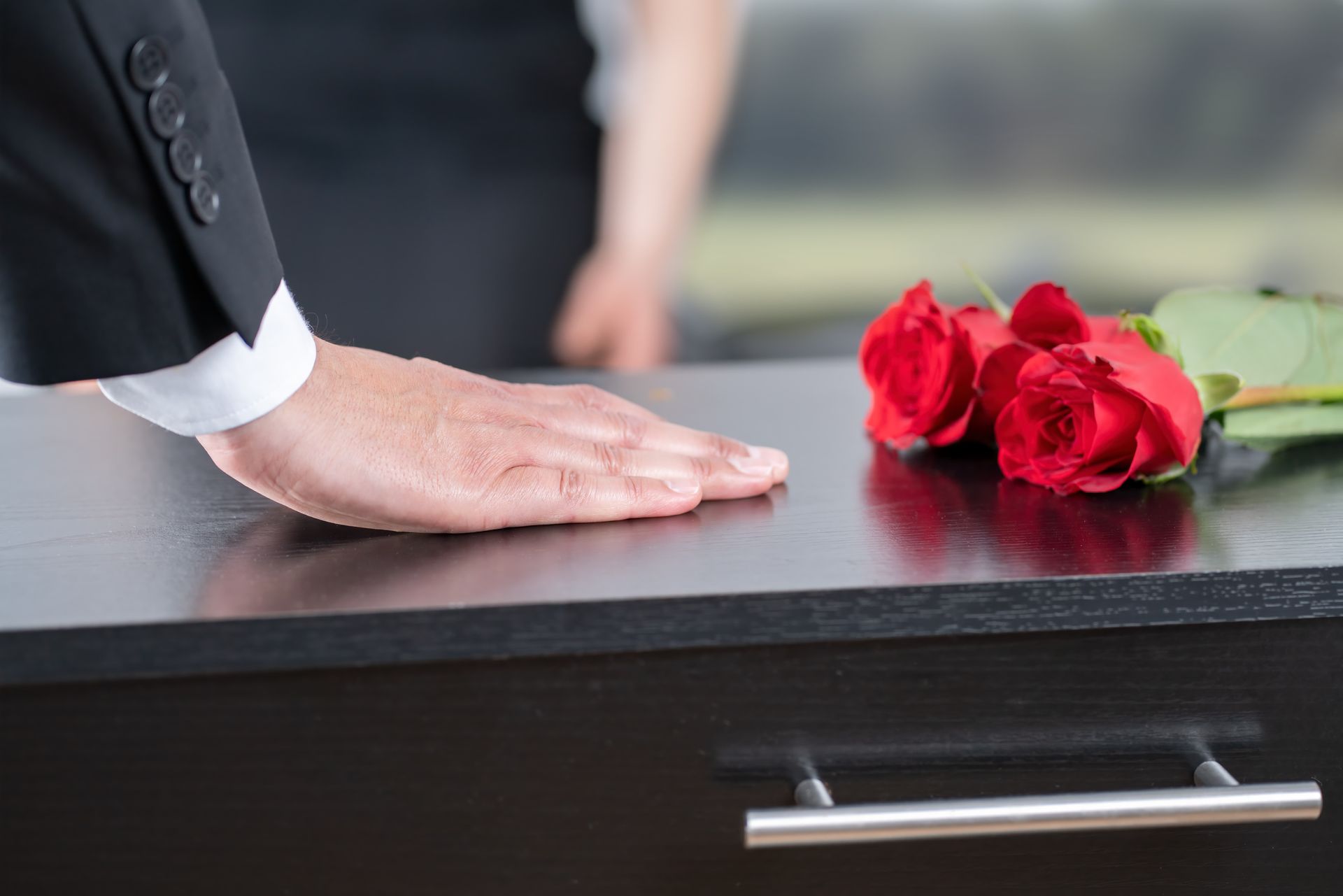 A man in a suit is sitting at a coffin at a funeral.
