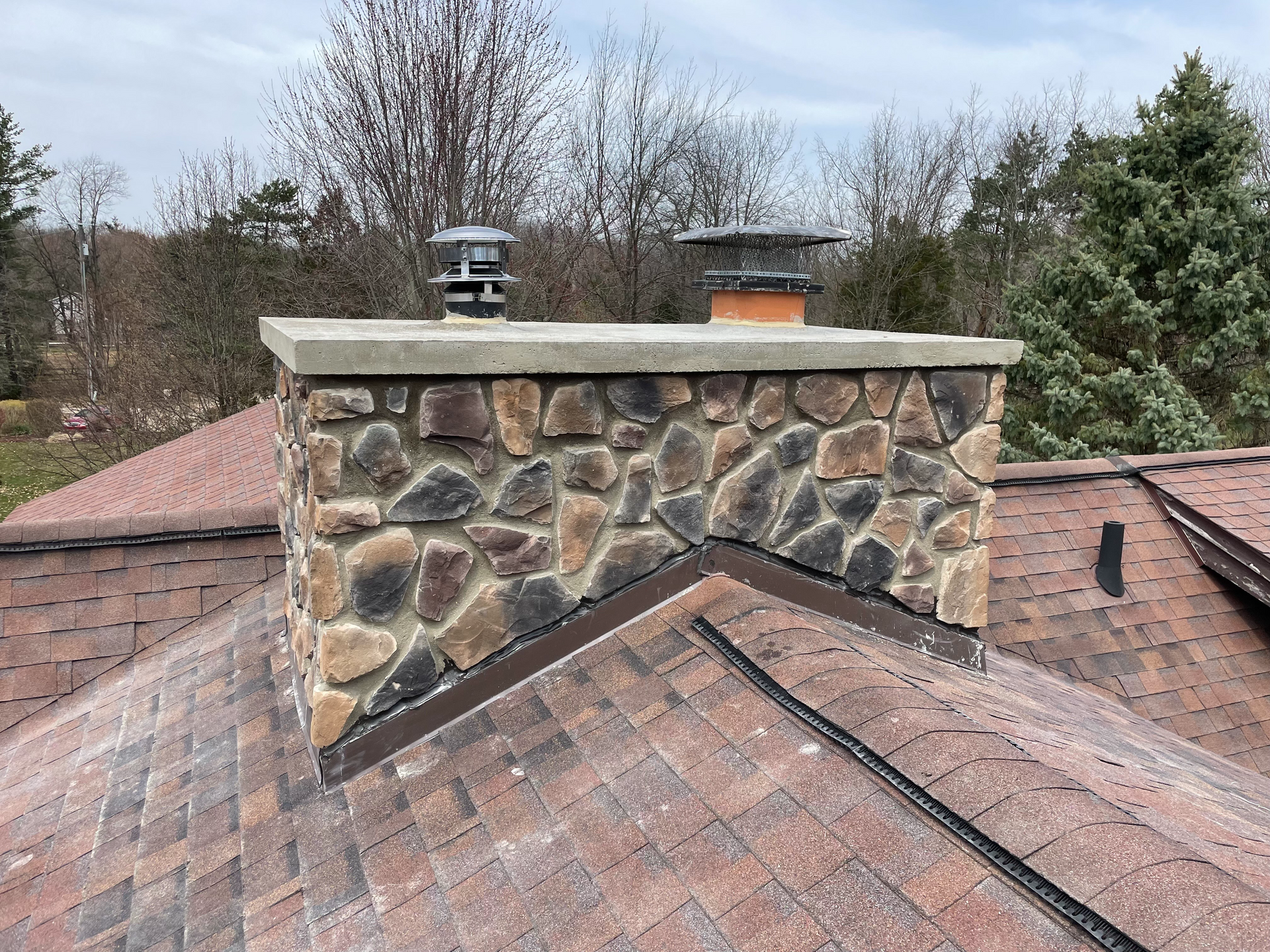 Stone chimney with a newly installed concrete crown and dual flues by EFD Masonry in Oakland County.
