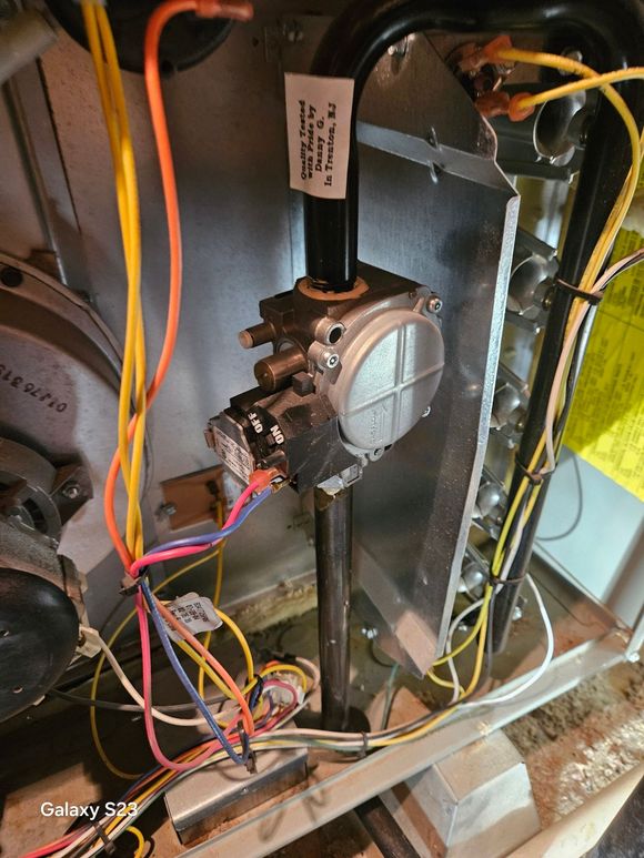 Internal view of a furnace showing the gas valve assembly with various colorful electrical wires and piping.