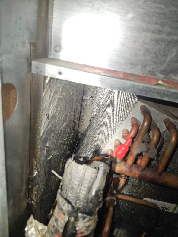 Close-up of a damaged HVAC evaporator coil showing black buildup, moisture, and a red cap on the refrigerant tubing.