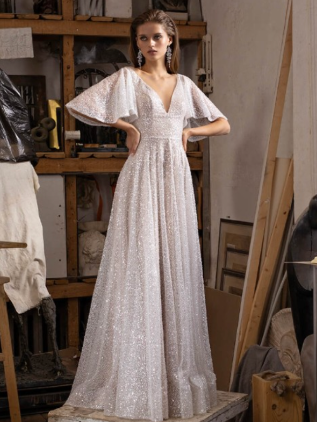 Woman in sparkling white gown with flared sleeves, posing in an art studio.