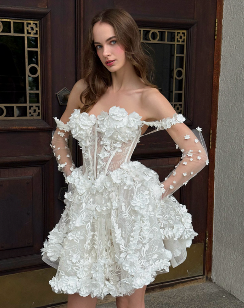 Woman in white floral dress stands in front of a dark wooden door.