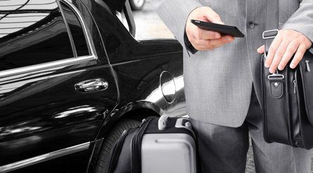 A man stood beside a shiny black car with a suitcase