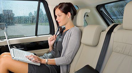 A woman in the back of a hire car on her laptop