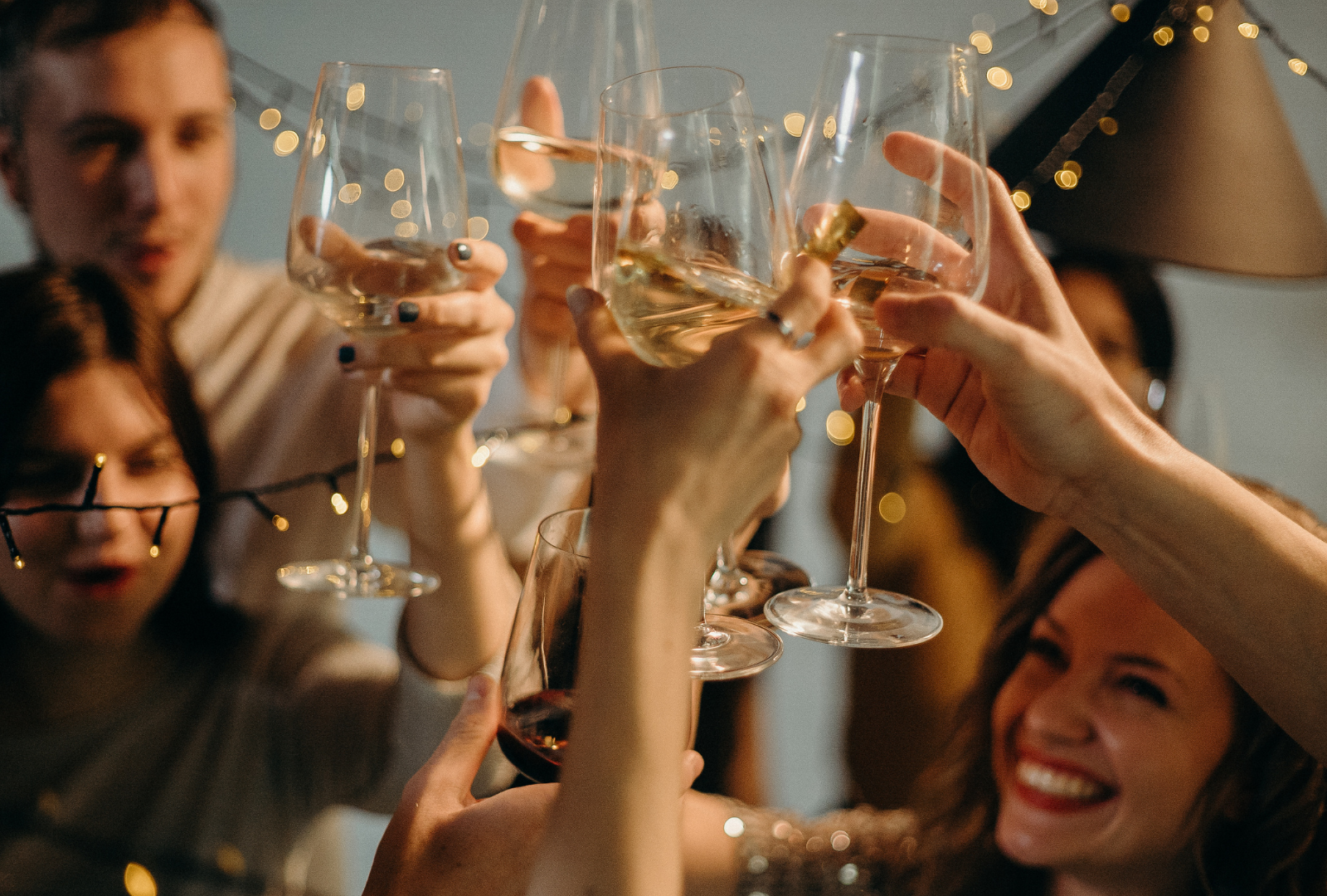 People at a party raising champagne flutes in a toast. Smiling faces with string lights in the background.