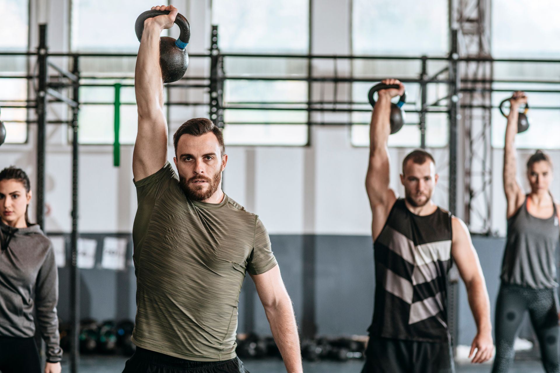 People in a gym lift kettlebells overhead. They are in a fitness class.